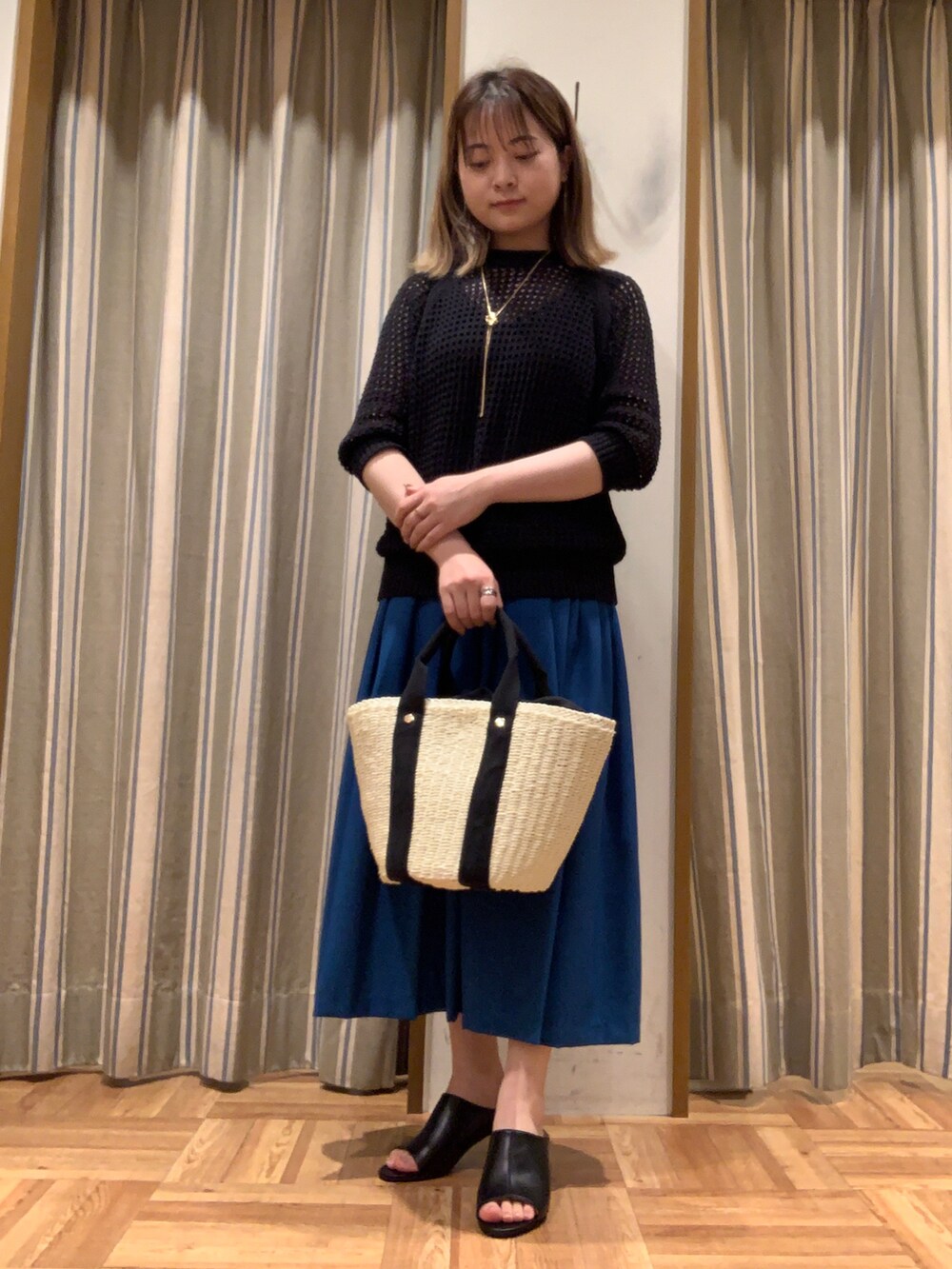 ブラック系のニット/セーター、ホワイト系のハンドバッグ、ブルー系のスカートを着用したレディースの春コーディネートの2枚目の写真