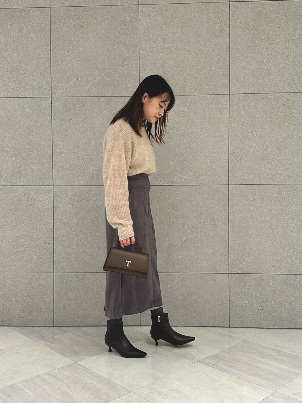 ベージュ系のニット/セーター、グレー系のスカート、ブラウン系のハンドバッグを着用したレディースの秋コーディネートの4枚目の写真