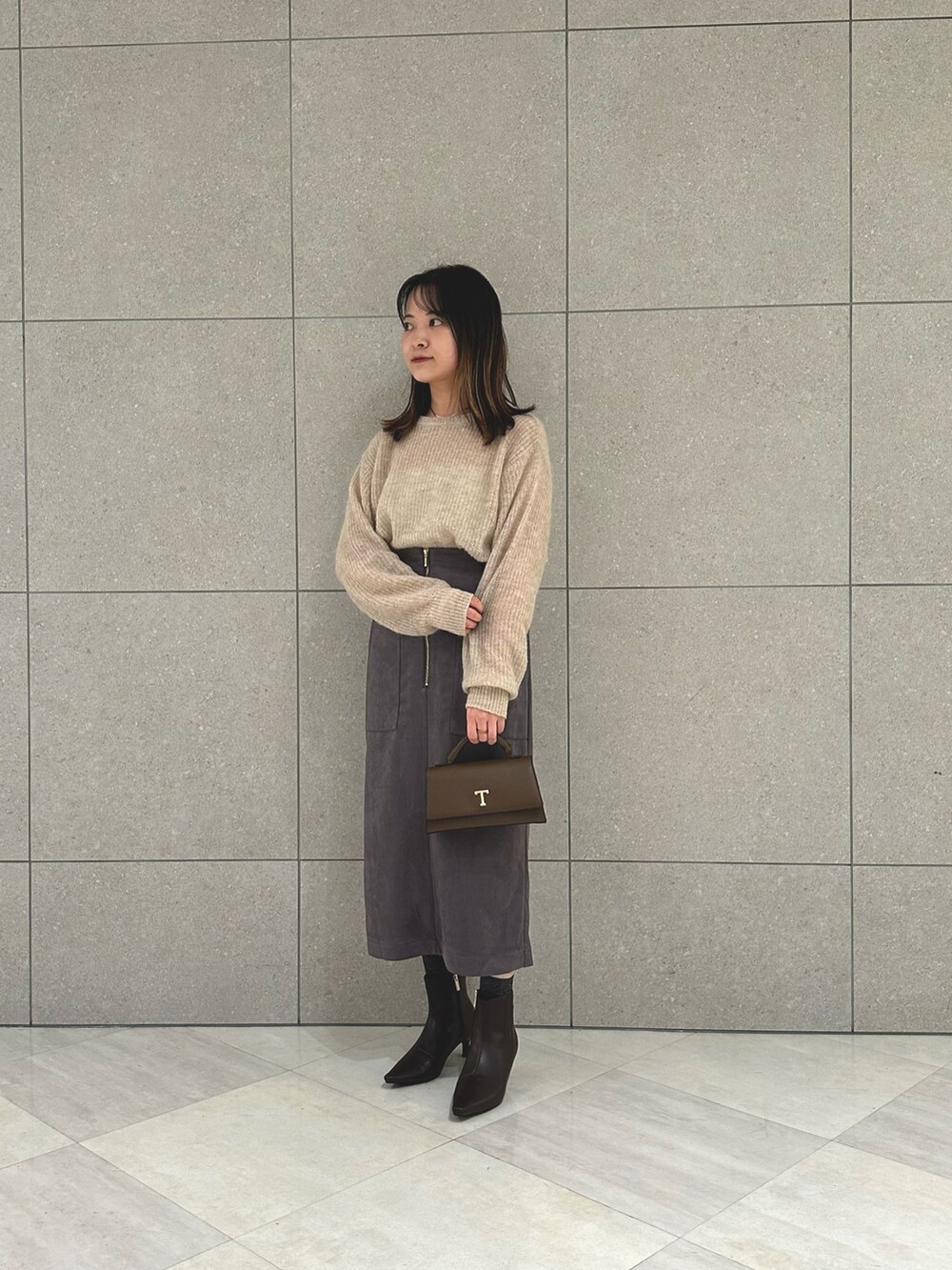 ベージュ系のニット/セーター、グレー系のスカート、ブラウン系のハンドバッグを着用したレディースの秋コーディネートの2枚目の写真