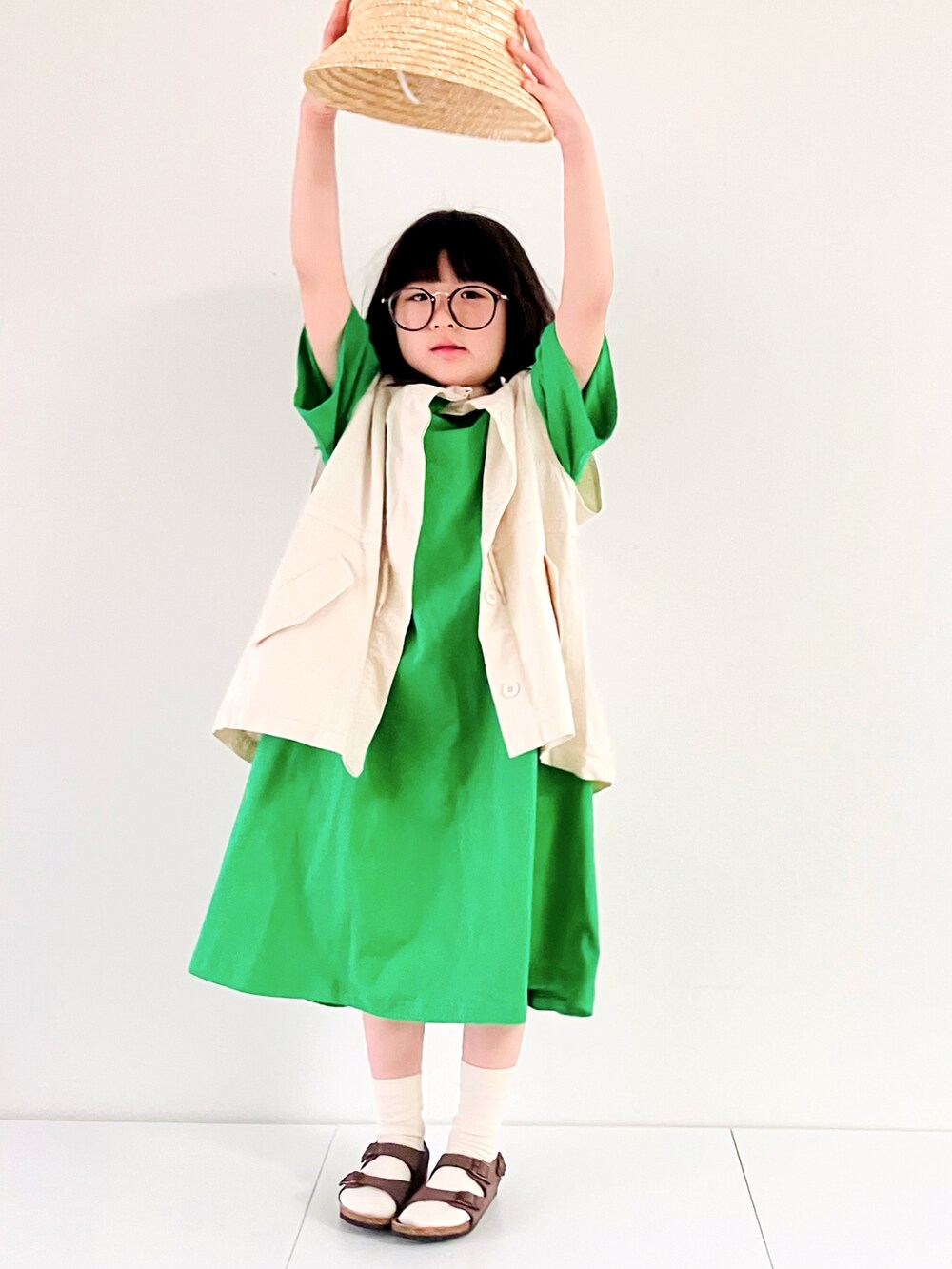 ホワイト系のベスト、グリーン系のワンピース、ブラウン系のサンダルを着用したキッズの春コーディネートの4枚目の写真