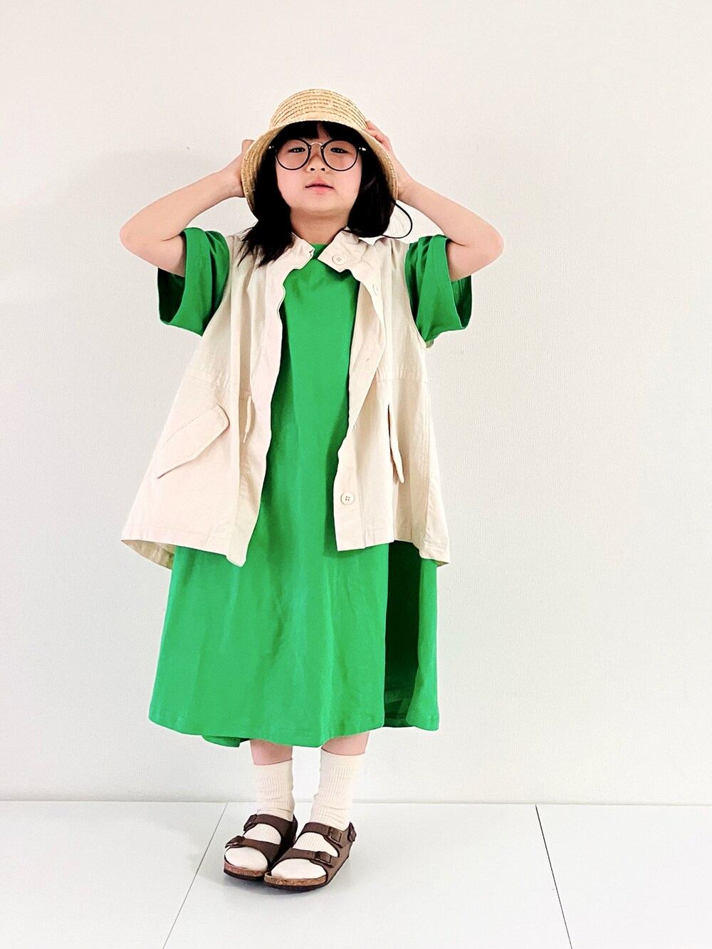 ホワイト系のベスト、グリーン系のワンピース、ブラウン系のサンダルを着用したキッズの春コーディネートの3枚目の写真