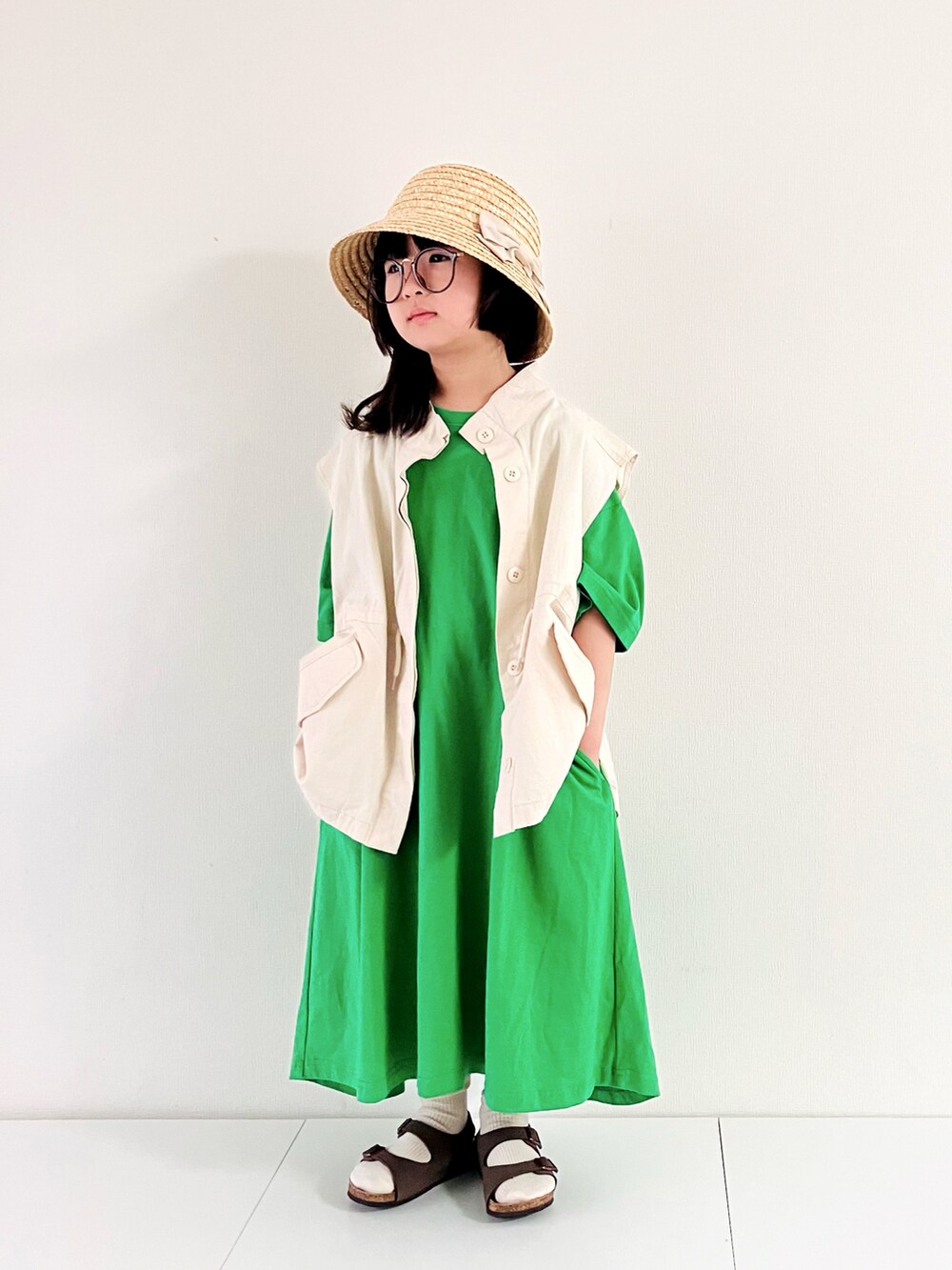 ホワイト系のベスト、グリーン系のワンピース、ブラウン系のサンダルを着用したキッズの春コーディネートの5枚目の写真