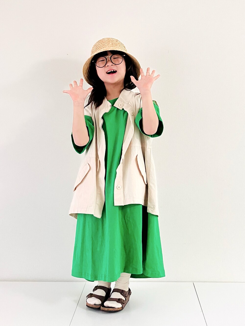ホワイト系のベスト、グリーン系のワンピース、ブラウン系のサンダルを着用したキッズの春コーディネートの2枚目の写真