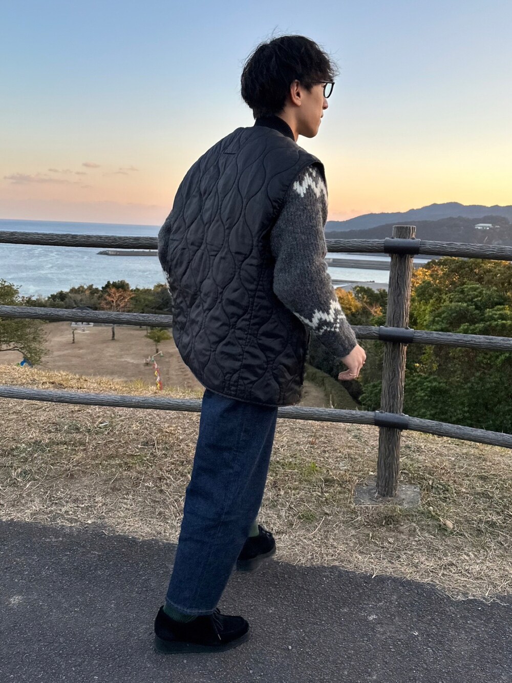 グレー系のニット/セーター、ブラック系のその他アウター、ブルー系のデニムパンツを着用したメンズの冬コーディネートの2枚目の写真