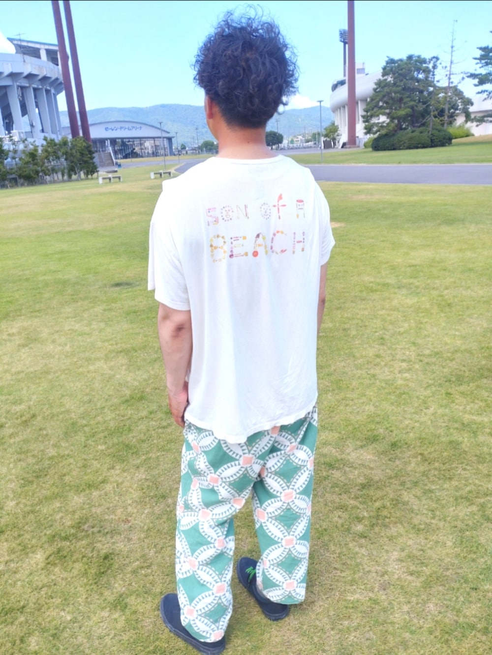 ホワイト系のTシャツ/カットソー、グリーン系のパンツ、ブラック系のスニーカーを着用したメンズの夏コーディネートの2枚目の写真