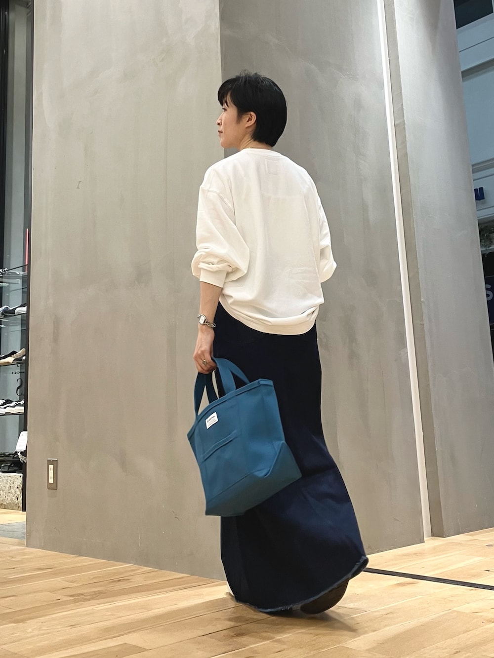 ブルー系のスカート、ブルー系のトートバッグ、ブラック系のスニーカーを着用したレディースの夏コーディネートの2枚目の写真