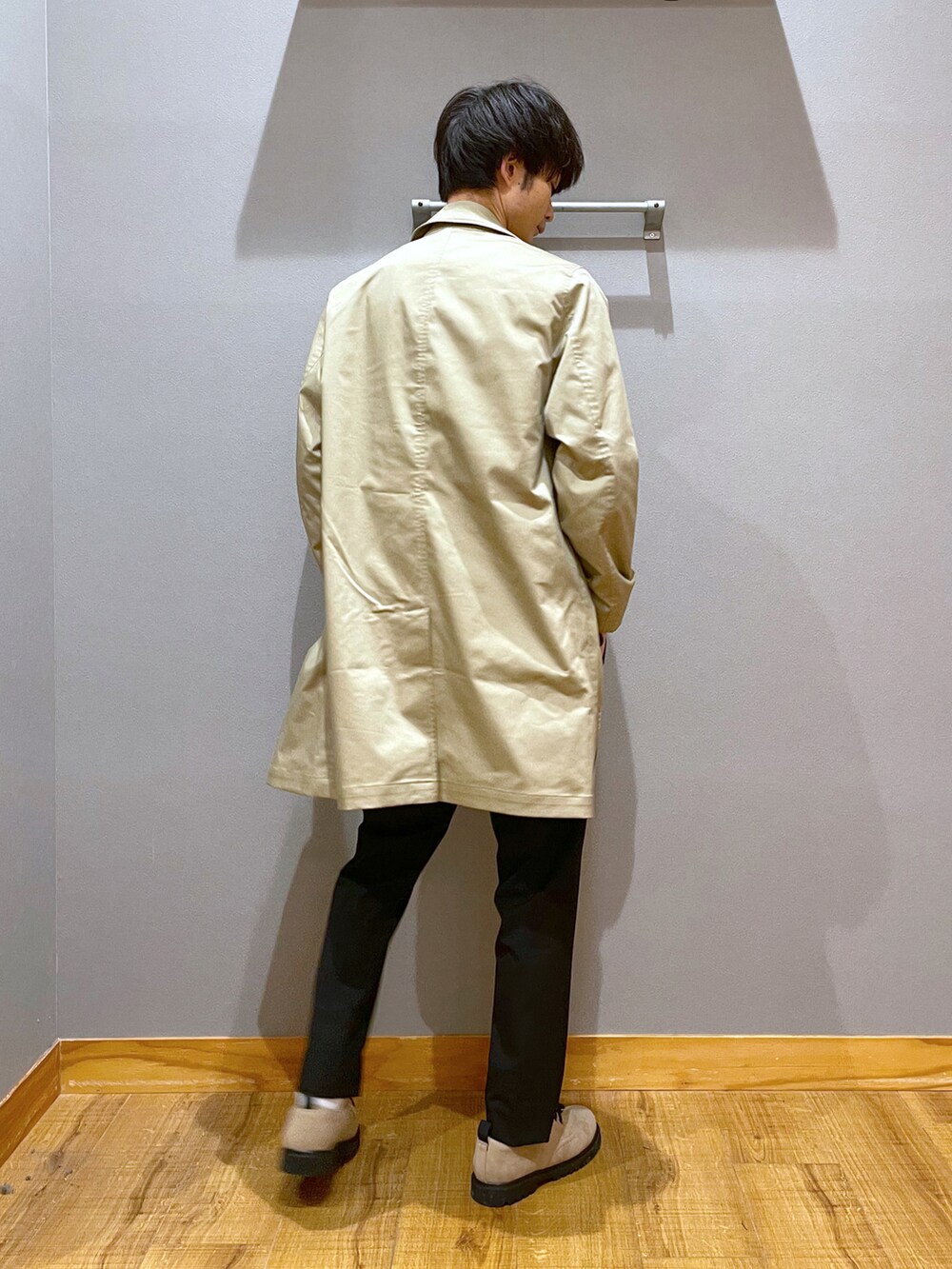 ブラック系のスラックス、ベージュ系のステンカラーコート、ブラウン系のTシャツ/カットソーを着用したメンズの春コーディネートの3枚目の写真