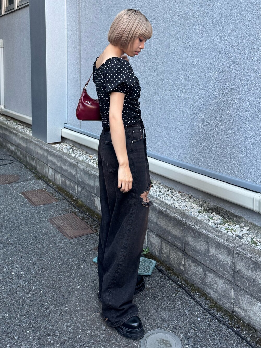 ブラック系のデニムパンツ、ブラック系のブーツ、レッド系のハンドバッグを着用したレディースの夏コーディネートの2枚目の写真