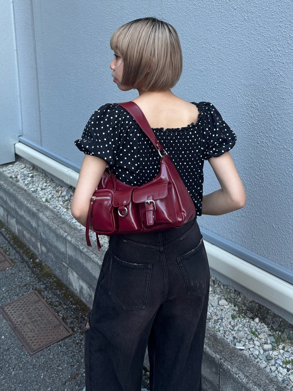 ブラック系のデニムパンツ、ブラック系のブーツ、レッド系のハンドバッグを着用したレディースの夏コーディネートの4枚目の写真