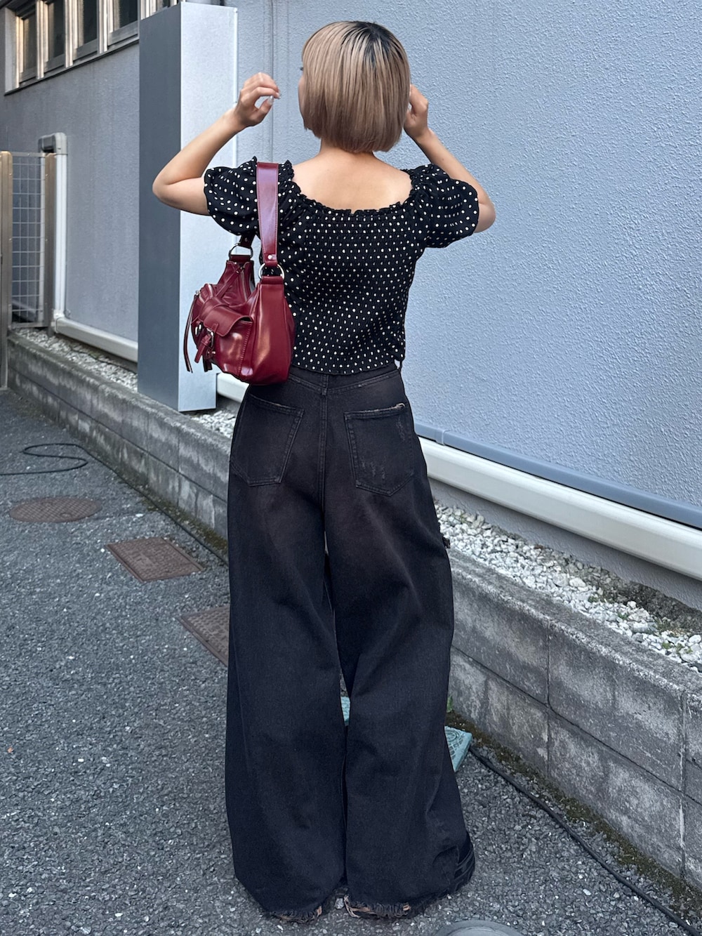 ブラック系のデニムパンツ、ブラック系のブーツ、レッド系のハンドバッグを着用したレディースの夏コーディネートの3枚目の写真