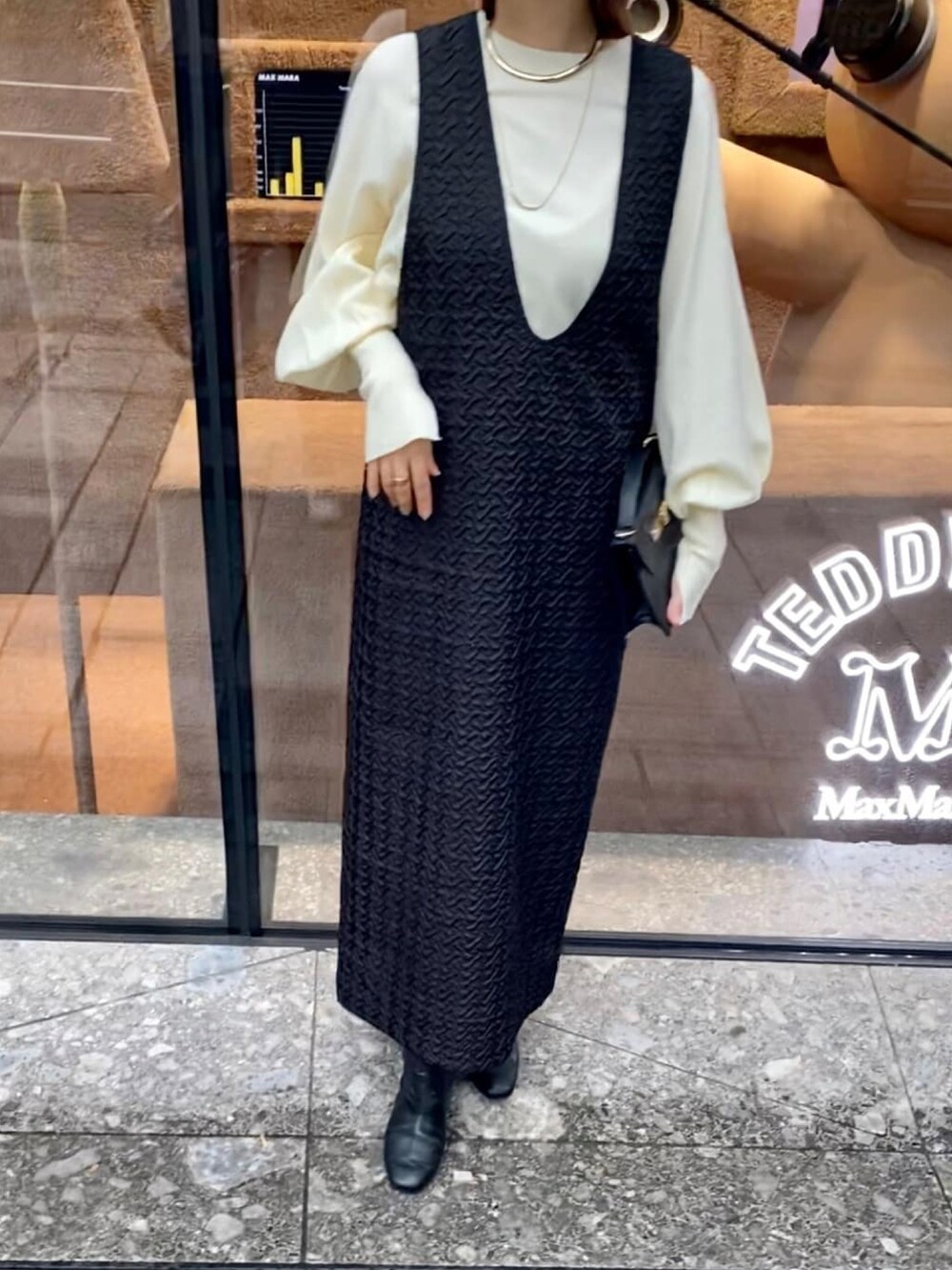 ブラック系のジャンパースカート、ホワイト系のニット/セーター、ブラック系のブーツを着用したレディースの秋コーディネートの4枚目の写真