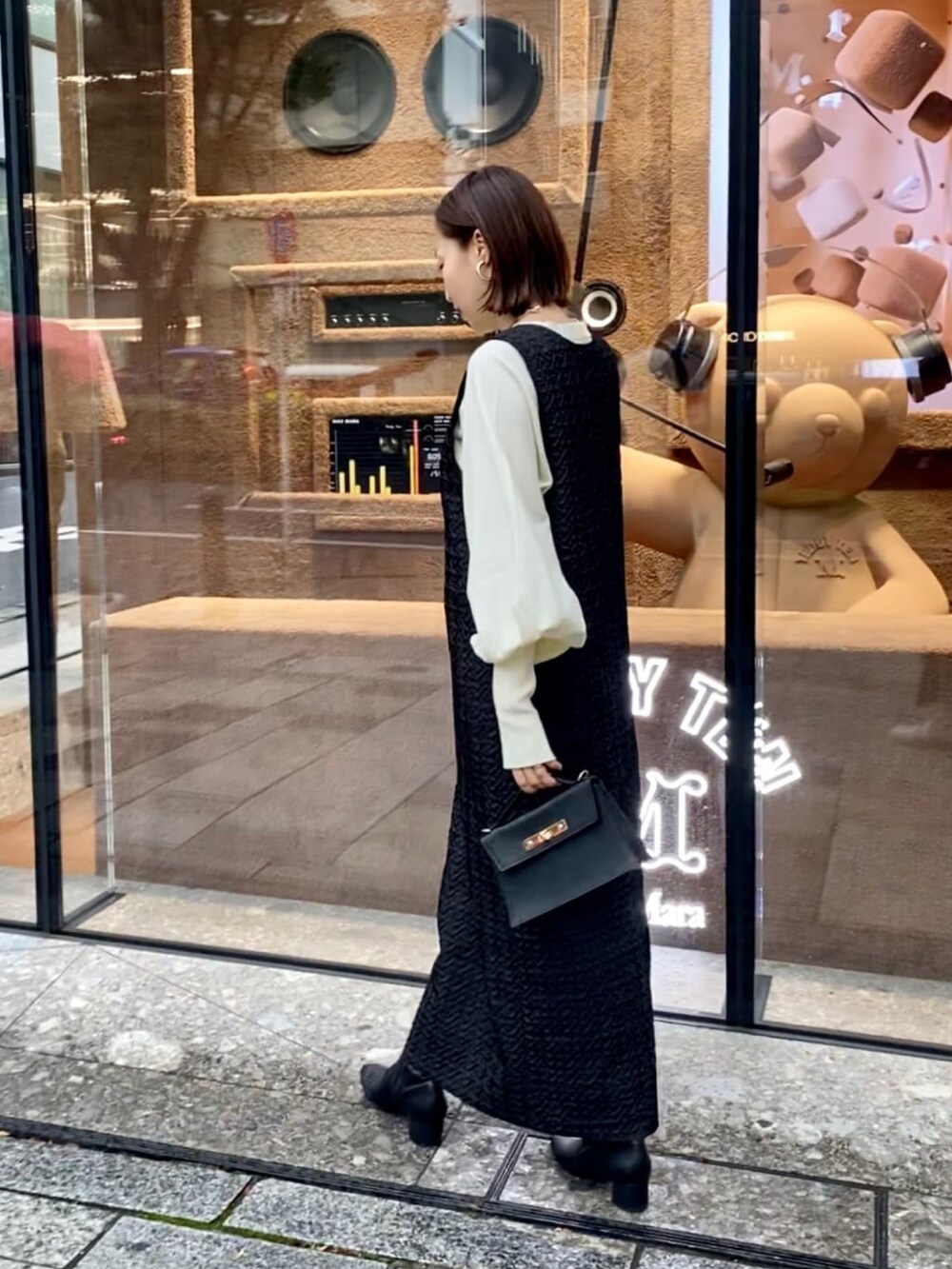 ブラック系のジャンパースカート、ホワイト系のニット/セーター、ブラック系のブーツを着用したレディースの秋コーディネートの2枚目の写真