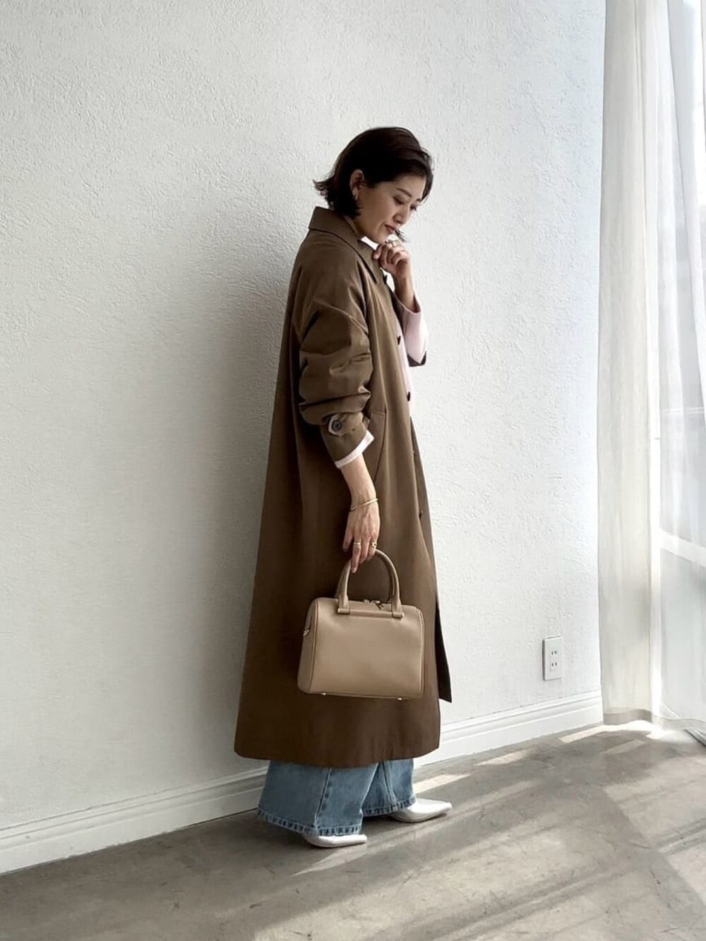 ピンク系のニット/セーター、ブラウン系のステンカラーコート、ブルー系のデニムパンツを着用したレディースの夏コーディネートの2枚目の写真