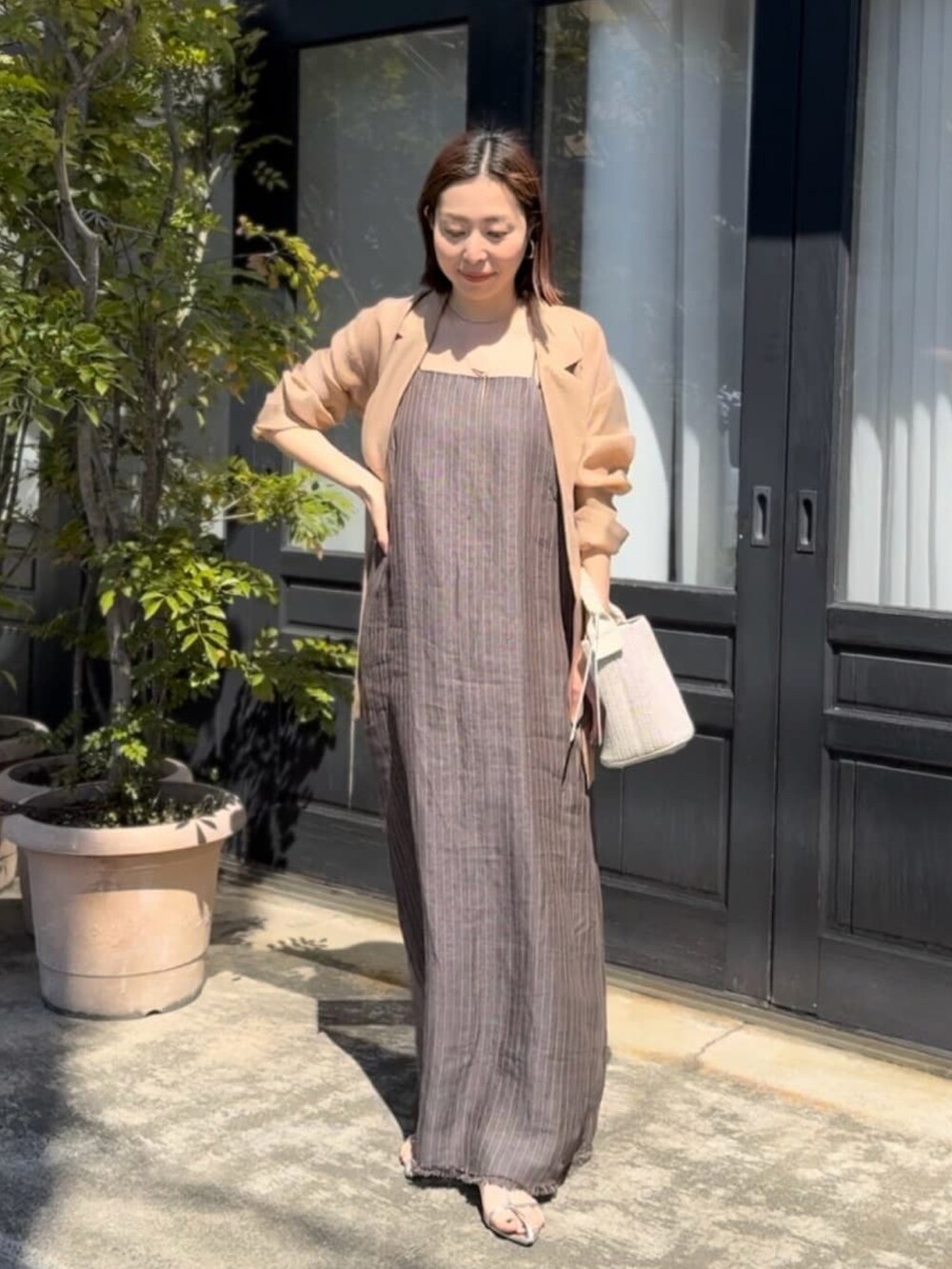 ブラック系のテーラードジャケット、ブラウン系のワンピース、シルバー系のサンダルを着用したレディースの春コーディネートの2枚目の写真