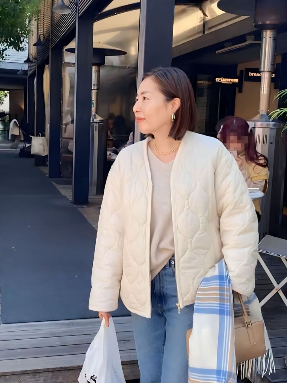 ブルー系のデニムパンツ、ホワイト系のダウンジャケット/コート、ベージュ系のニット/セーターを着用したレディースの秋コーディネートの2枚目の写真