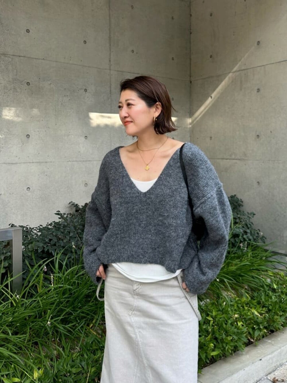 グレー系のニット/セーター、グレー系のデニムスカート、ホワイト系のTシャツ/カットソーを着用したレディースの秋コーディネートの4枚目の写真