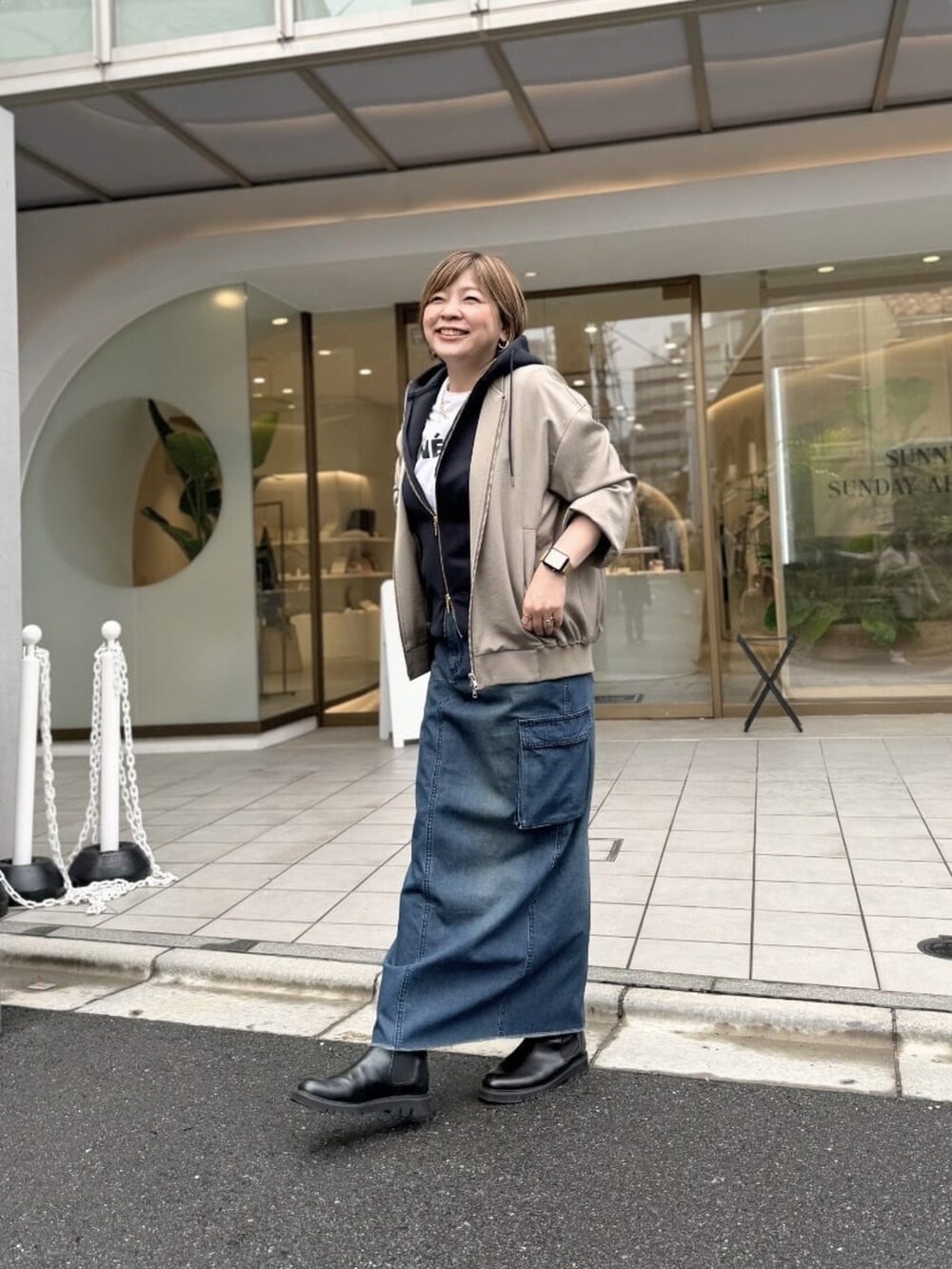 ブラック系のパーカー、ブルー系のデニムスカート、ブラック系のブーツを着用したレディースの秋コーディネートの2枚目の写真