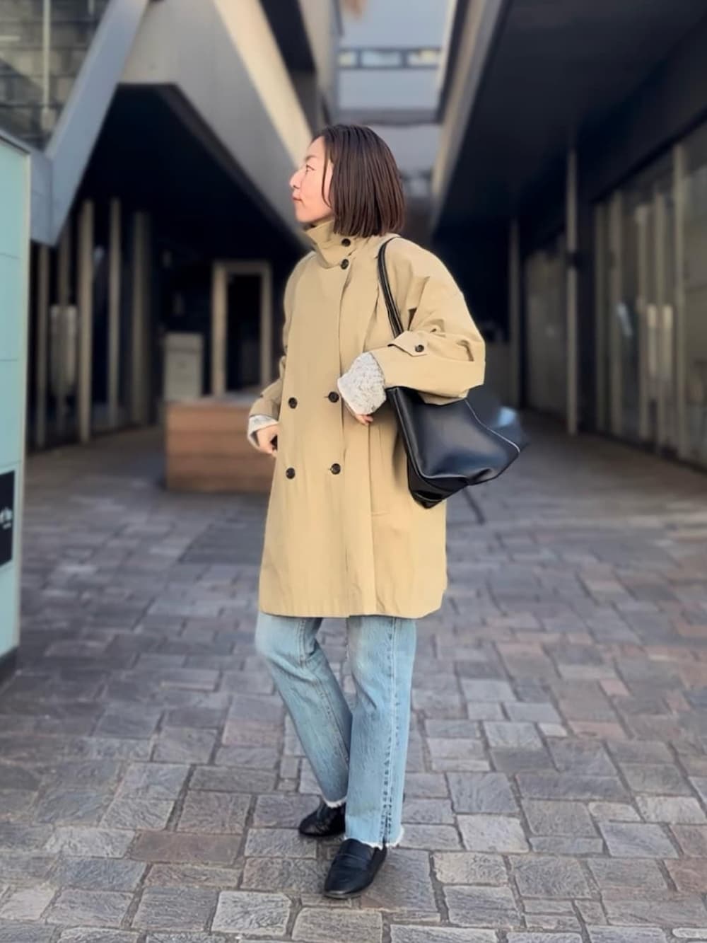 ベージュ系のトレンチコート、ブルー系のデニムパンツ、ブラック系のローファーを着用したレディースの冬コーディネートの3枚目の写真