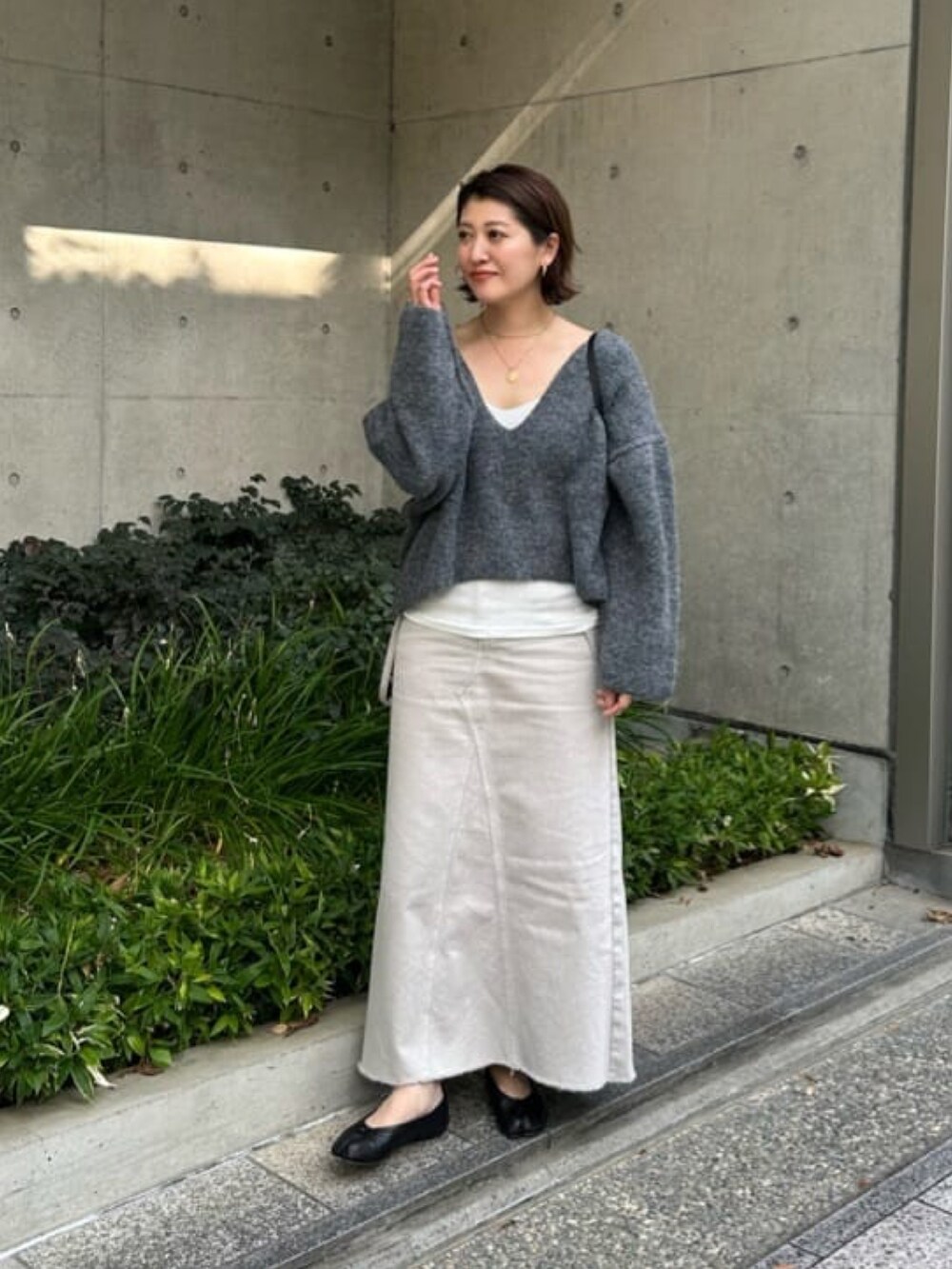 グレー系のニット/セーター、グレー系のデニムスカート、ホワイト系のTシャツ/カットソーを着用したレディースの秋コーディネートの2枚目の写真