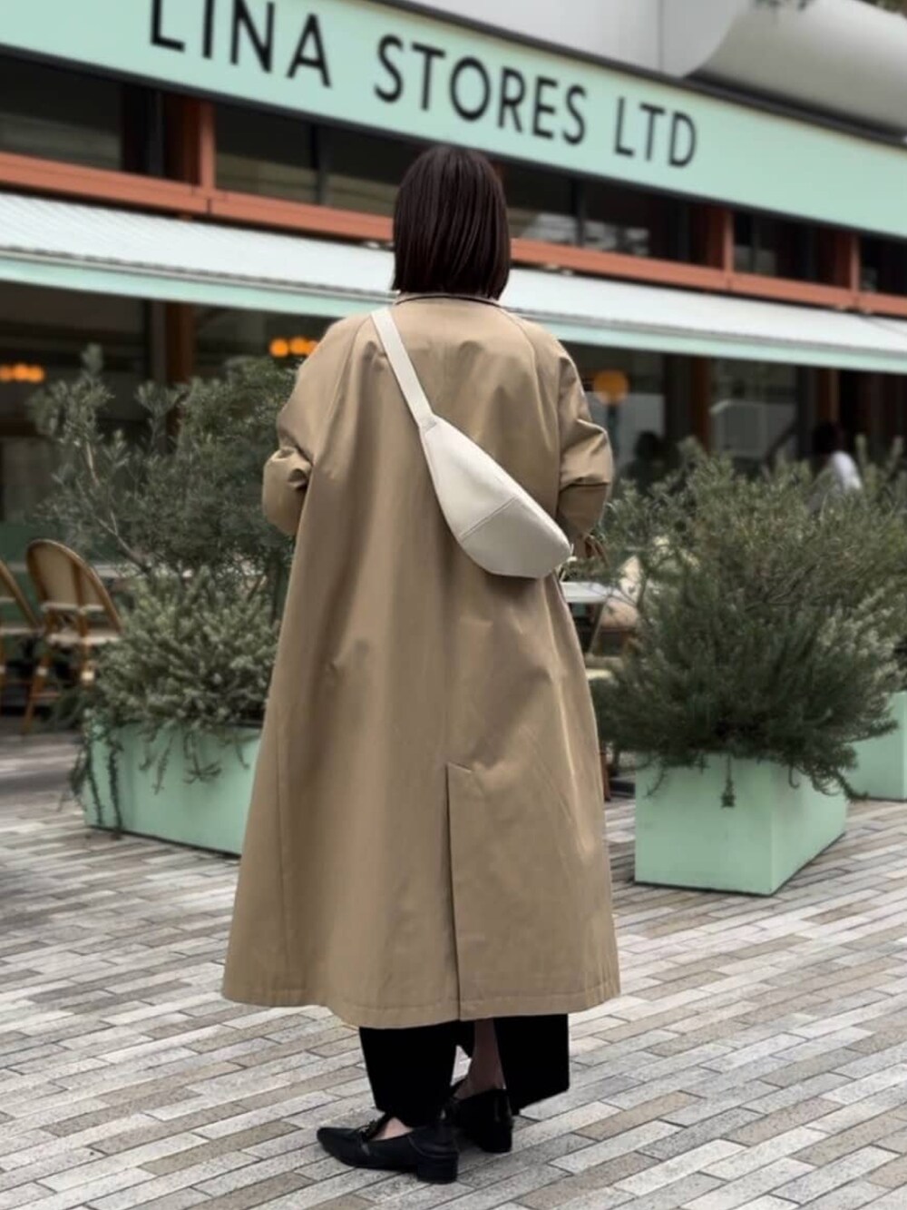 ベージュ系のステンカラーコート、ホワイト系のボディバッグ/ウエストポーチ、ブラック系のワンピースを着用したレディースの冬コーディネートの3枚目の写真