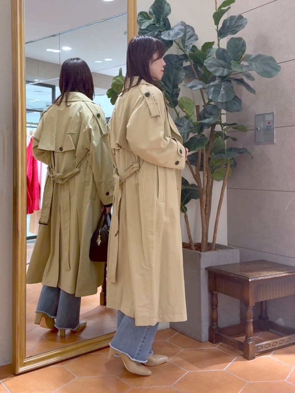 ベージュ系のトレンチコート、ブラック系のボストンバッグ、ブルー系のデニムパンツを着用したレディースの冬コーディネートの3枚目の写真