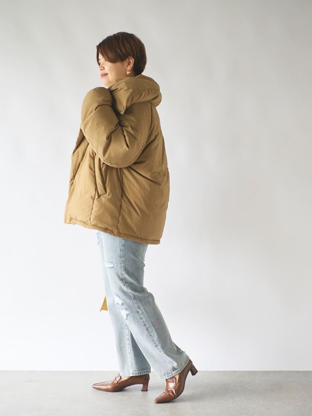 ブラウン系のダウンジャケット/コート、ブルー系のデニムパンツ、ブラウン系のローファーを着用したレディースの秋コーディネートの2枚目の写真