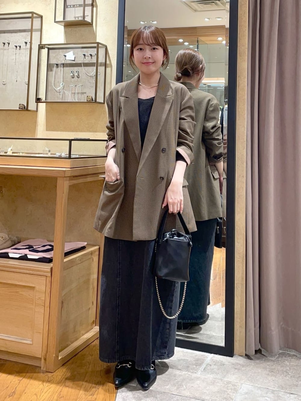 ブラウン系のテーラードジャケット、ブラック系のワンピース、ブラック系のハンドバッグを着用したレディースの秋コーディネートの2枚目の写真