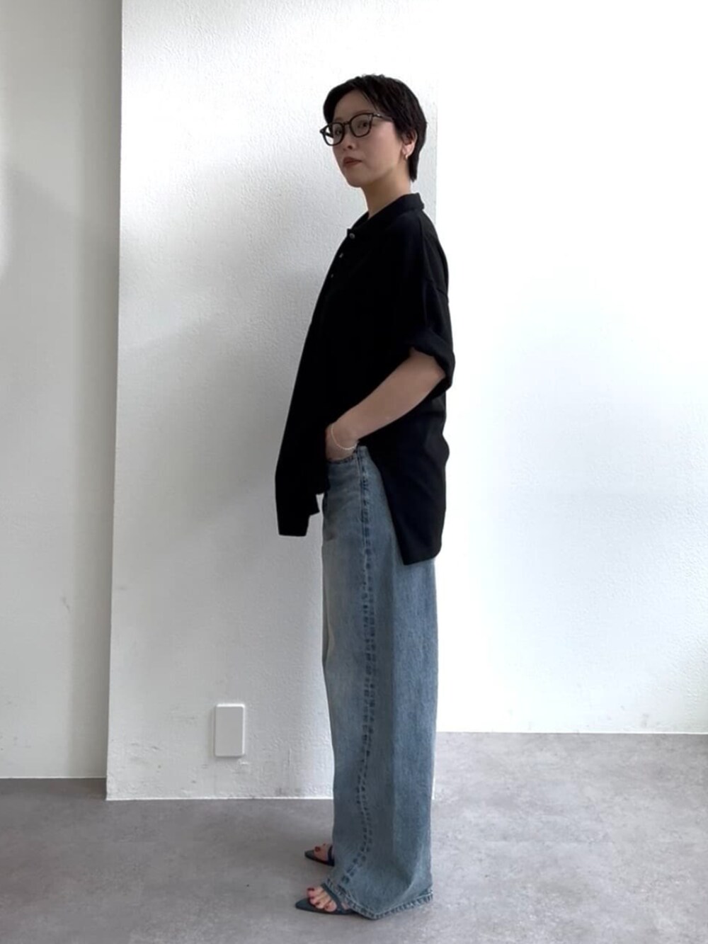 ブルー系のデニムパンツ、ブルー系のサンダル、ブラック系のポロシャツを着用したレディースの春コーディネートの3枚目の写真