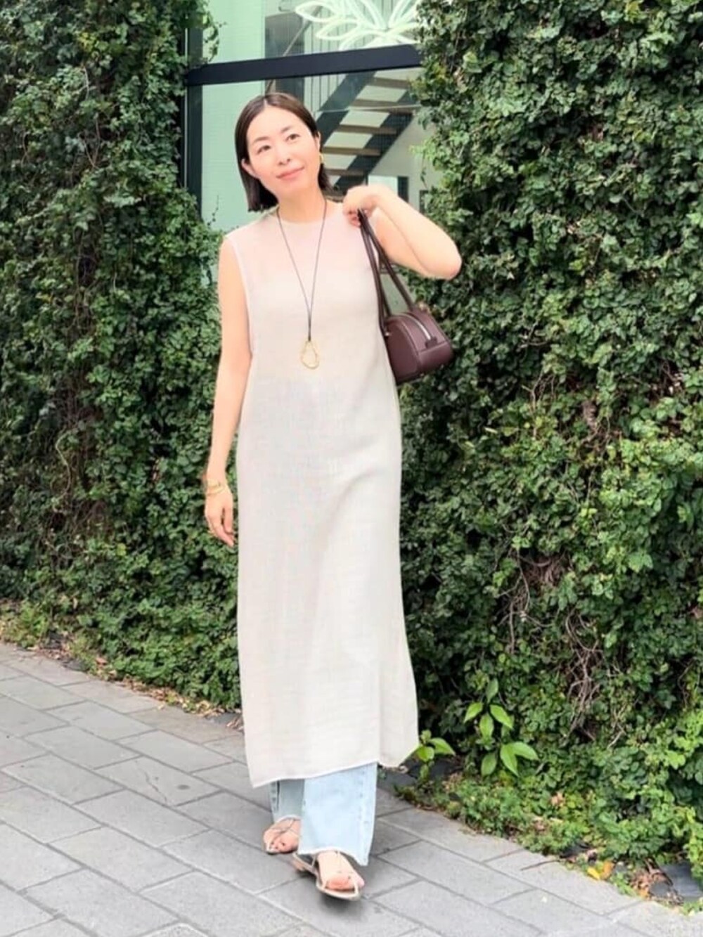 ブラウン系のショルダーバッグ、ベージュ系のワンピース、ブルー系のデニムパンツを着用したレディースの夏コーディネートの2枚目の写真