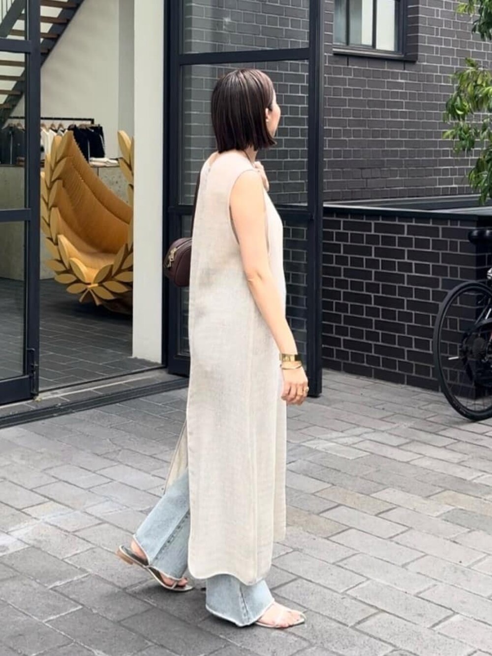 ブラウン系のショルダーバッグ、ベージュ系のワンピース、ブルー系のデニムパンツを着用したレディースの夏コーディネートの3枚目の写真