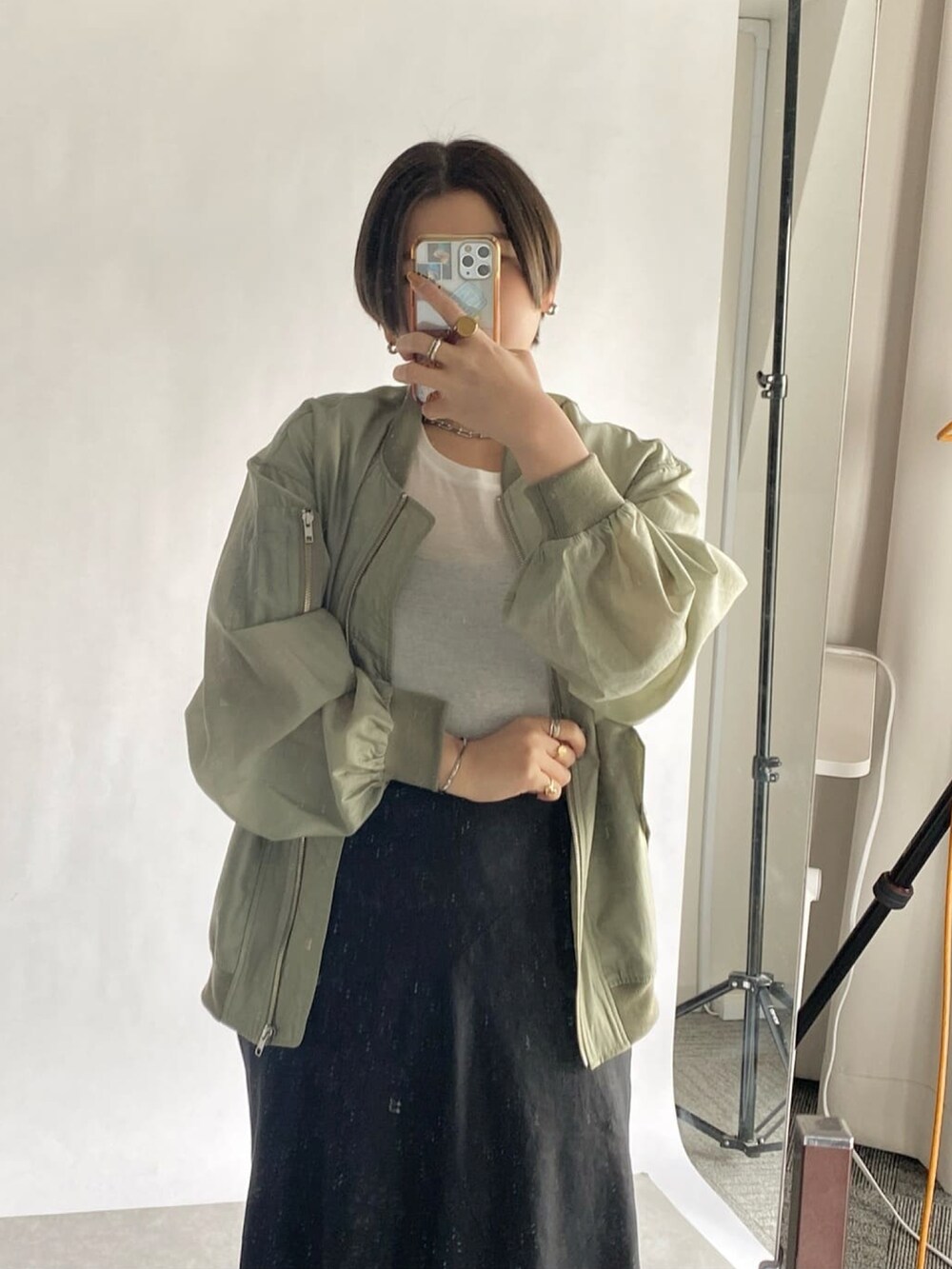 ブラック系のスカート、シルバー系のサンダル、ベージュ系のブルゾンを着用したレディースの春コーディネートの2枚目の写真