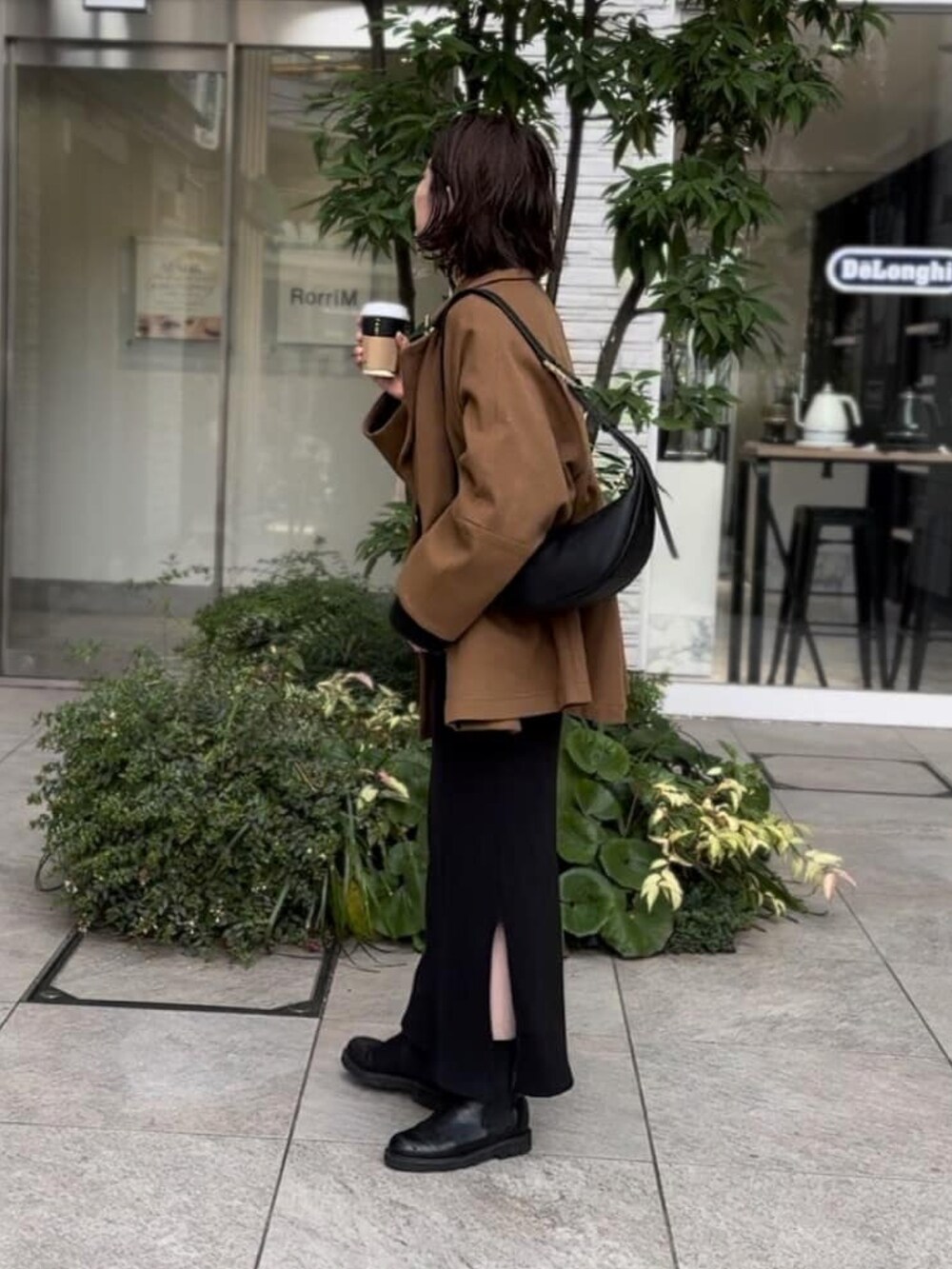 イエロー系のピーコート、ブラック系のワンピース、ブラック系のブーツを着用したレディースの冬コーディネートの2枚目の写真