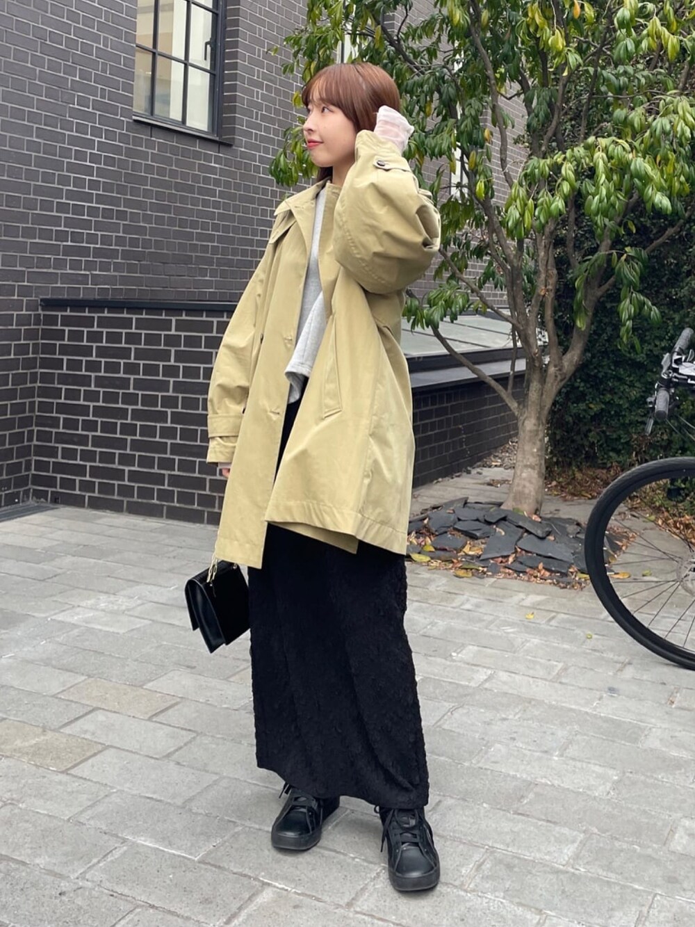 ベージュ系のトレンチコート、グレー系のスウェット、ブラック系のスカートを着用したレディースの冬コーディネートの2枚目の写真