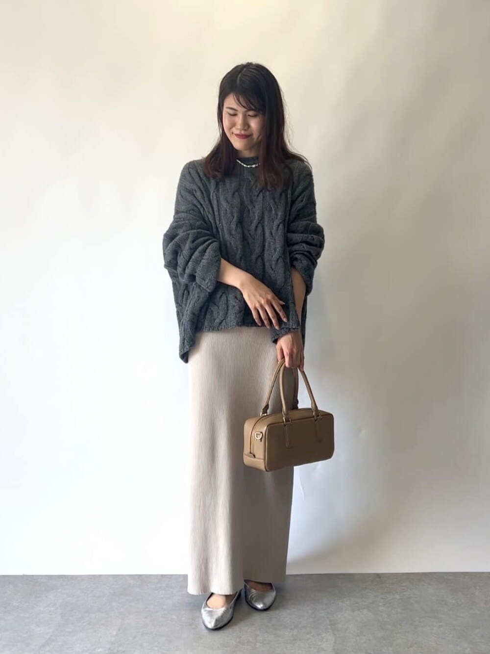 ベージュ系のスカート、グレー系のニット/セーター、イエロー系のボストンバッグを着用したレディースの秋コーディネートの2枚目の写真