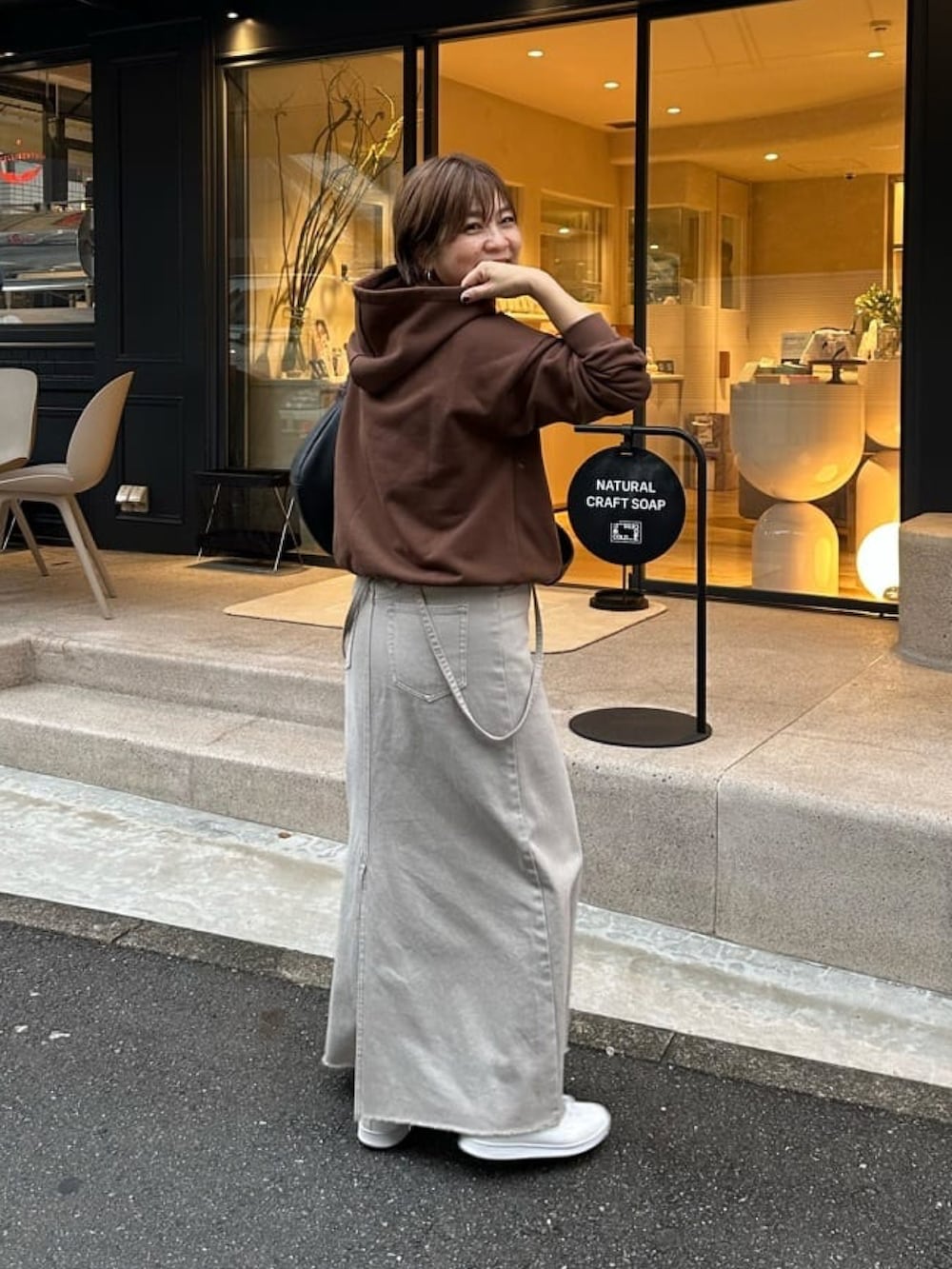 グレー系のデニムスカート、ブラック系のボディバッグ/ウエストポーチ、ブラウン系のパーカーを着用したレディースの秋コーディネートの3枚目の写真