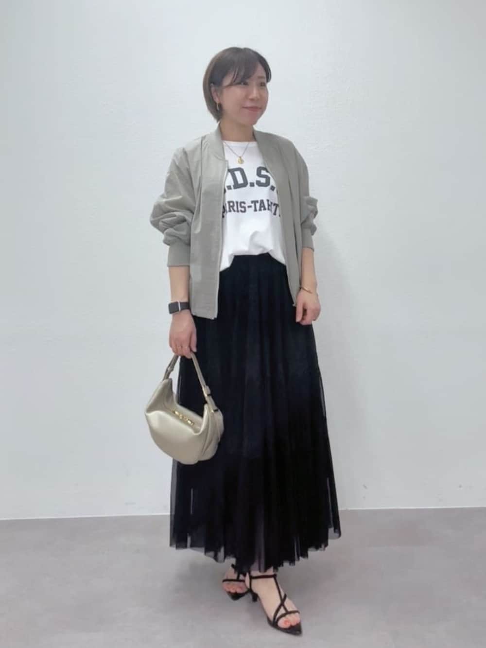 ブラック系のサンダル、ゴールド系のショルダーバッグ、グリーン系のブルゾンを着用したレディースの春コーディネートの3枚目の写真