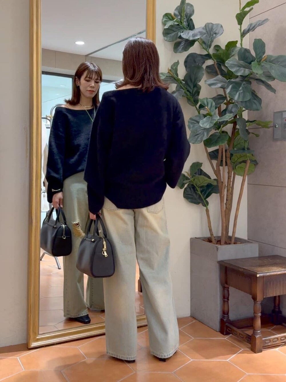 ブラック系のニット/セーター、ブラック系のボストンバッグ、ブルー系のデニムパンツを着用したレディースの秋コーディネートの3枚目の写真