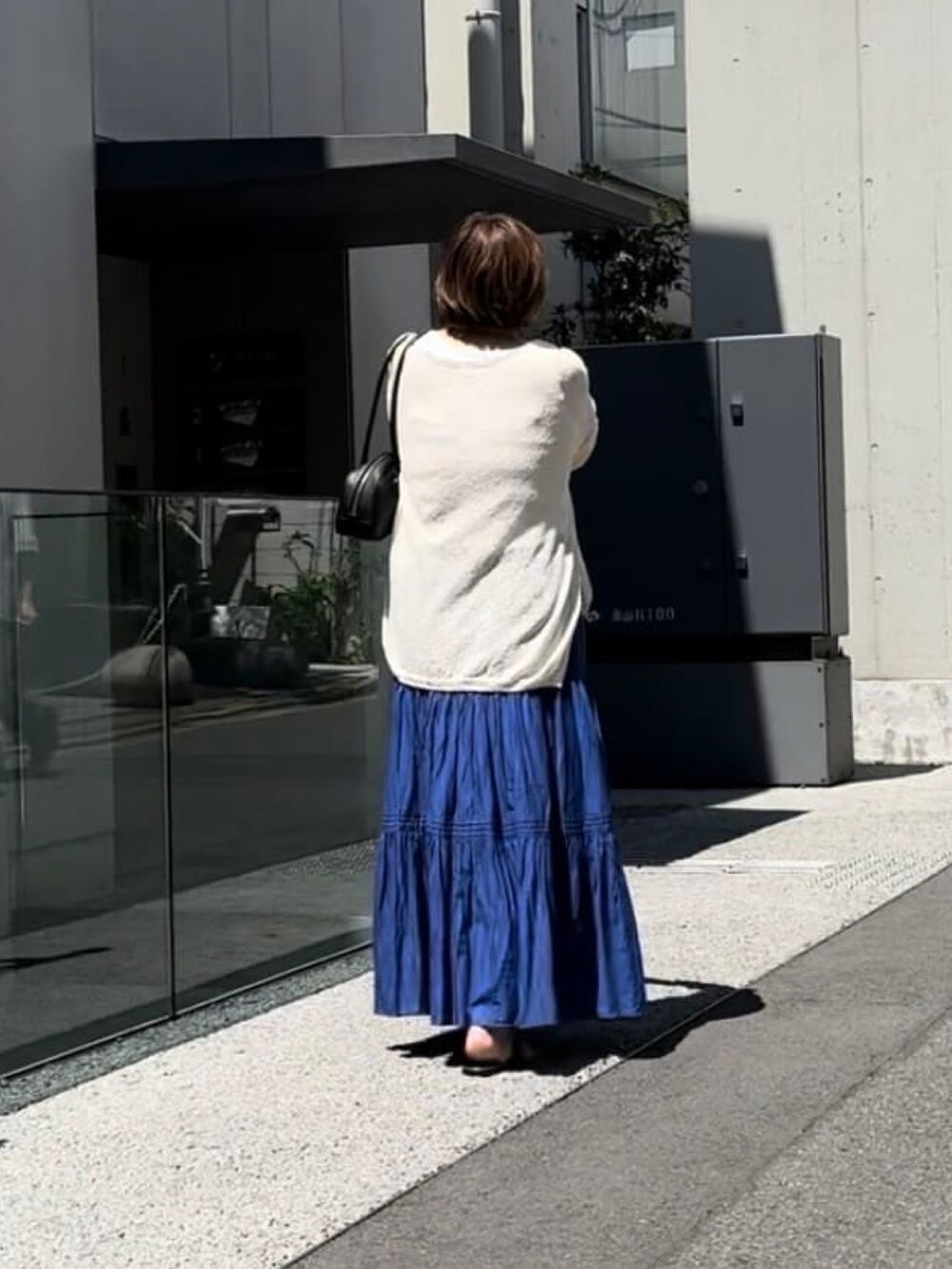 ブルー系のスカート、ホワイト系のニット/セーター、ブラック系のショルダーバッグを着用したレディースの春コーディネートの3枚目の写真