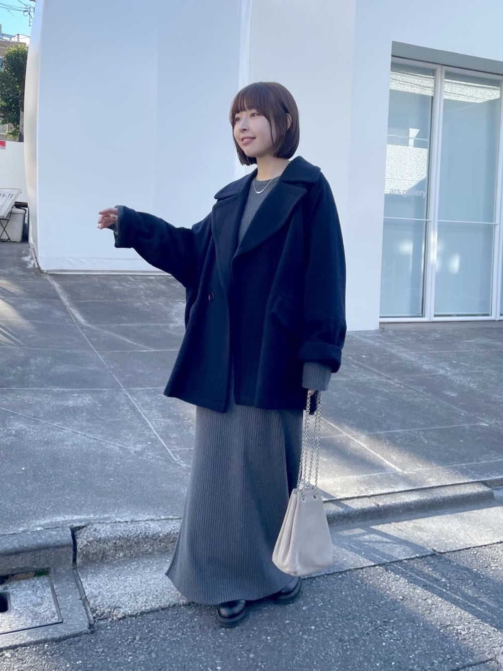 イエロー系のピーコート、グレー系のワンピース、ベージュ系のショルダーバッグを着用したレディースの冬コーディネートの2枚目の写真