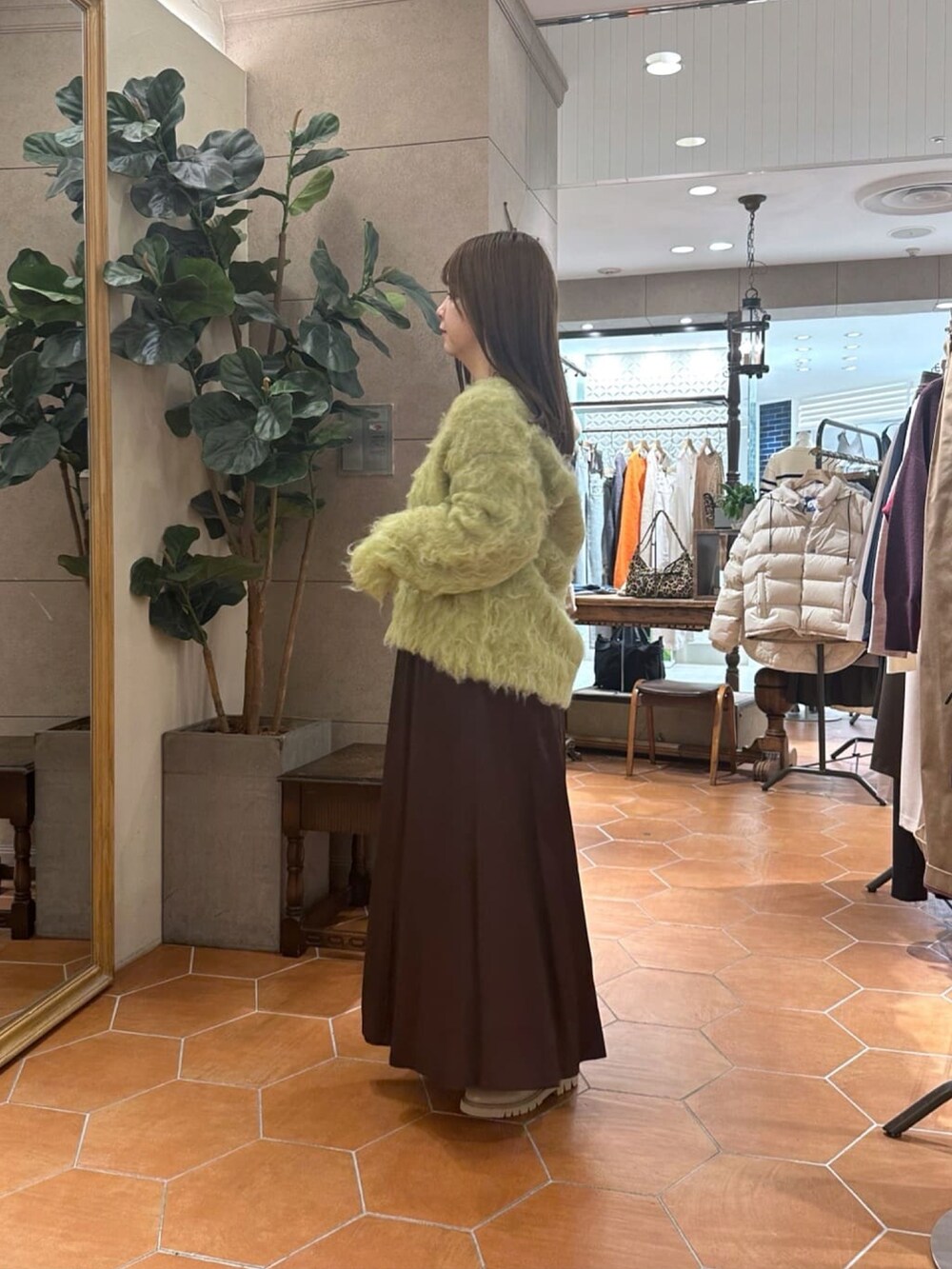 グリーン系のニット/セーター、ブラウン系のスカート、イエロー系のボストンバッグを着用したレディースの冬コーディネートの2枚目の写真