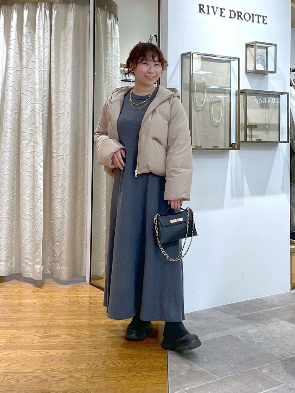 ブラック系のダウンジャケット/コート、グレー系のワンピース、ブラック系のブーツを着用したレディースの冬コーディネートの2枚目の写真