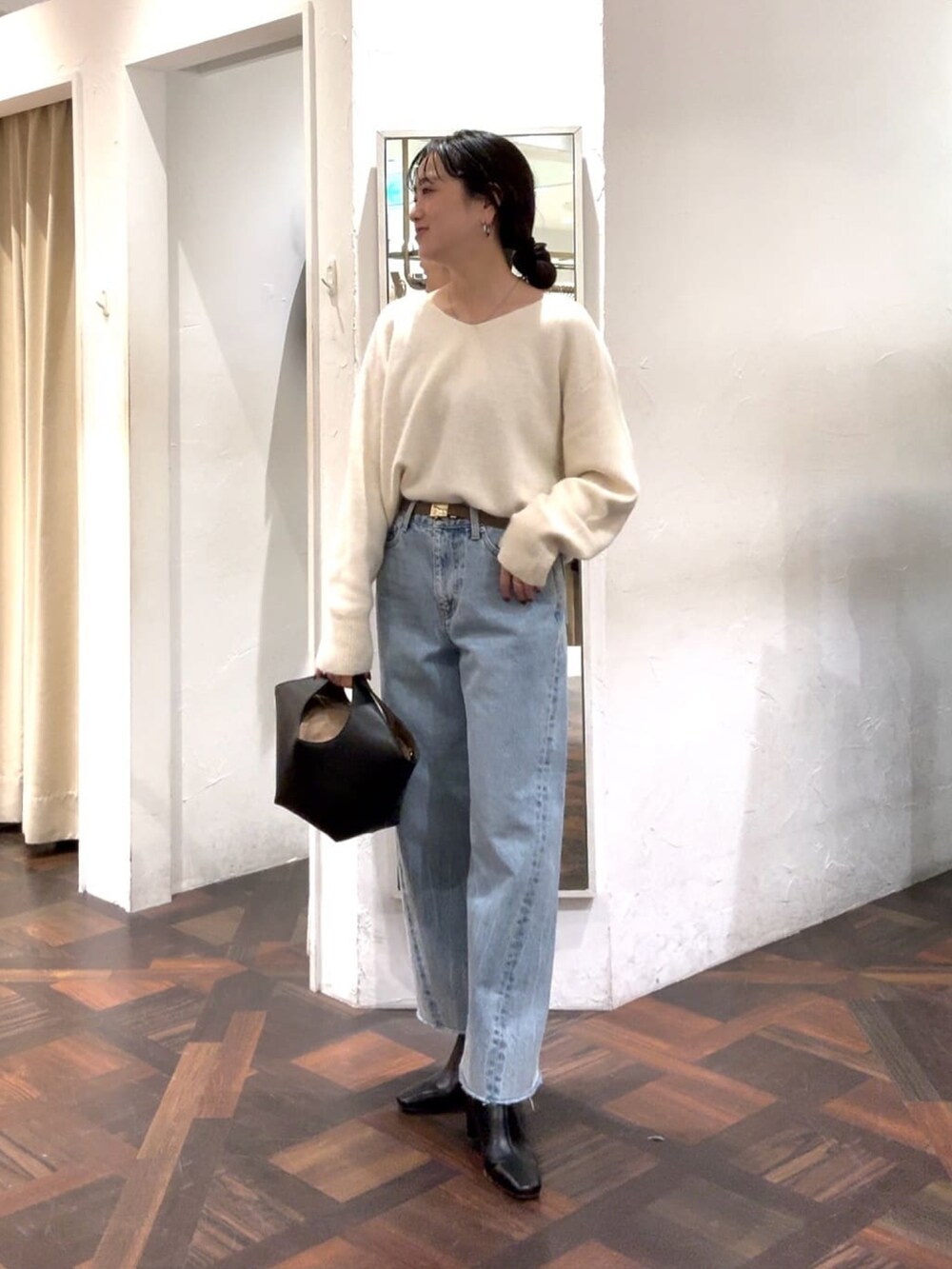 ホワイト系のニット/セーター、ブラック系のハンドバッグ、ブルー系のデニムパンツを着用したレディースの冬コーディネートの3枚目の写真