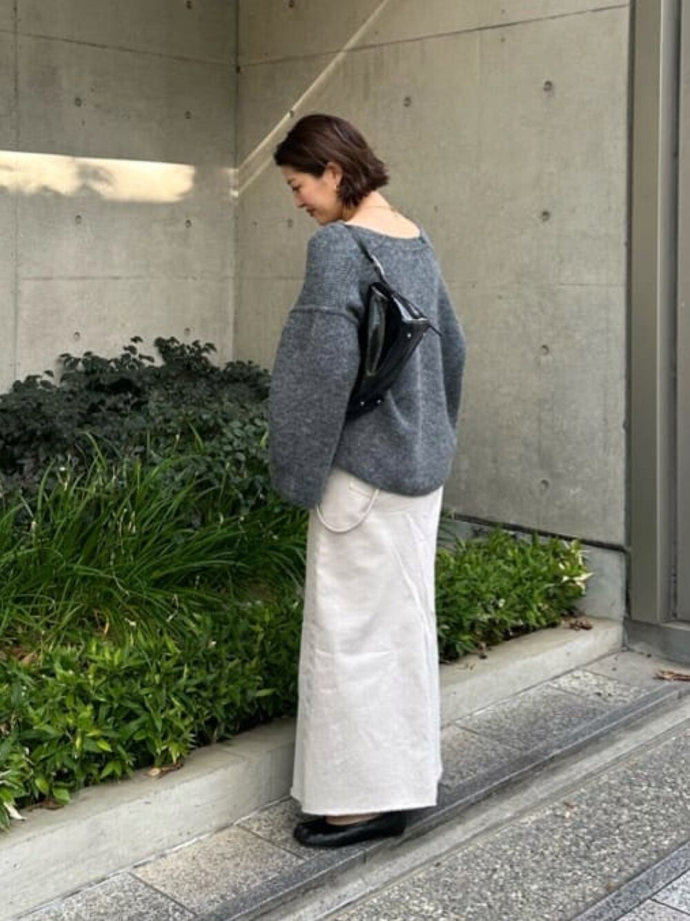 グレー系のニット/セーター、グレー系のデニムスカート、ホワイト系のTシャツ/カットソーを着用したレディースの秋コーディネートの3枚目の写真