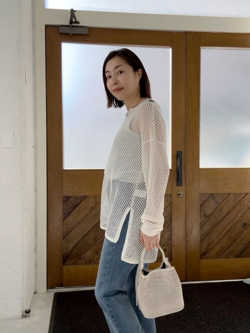 ホワイト系のニット/セーター、ホワイト系のハンドバッグ、ブルー系のデニムパンツを着用したレディースの冬コーディネートの2枚目の写真