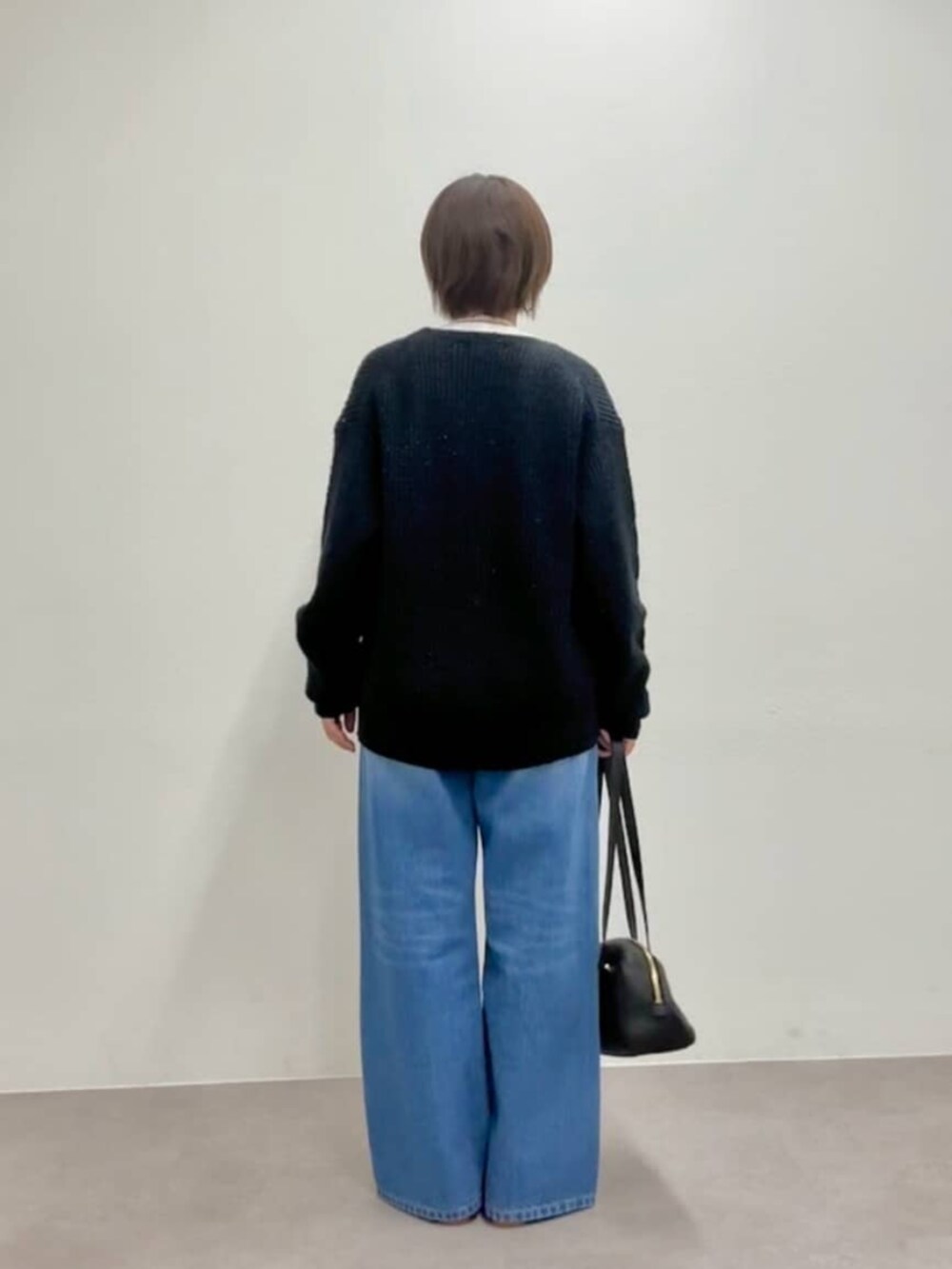 ブラック系のショルダーバッグ、グレー系のパンプス、ブルー系のデニムパンツを着用したレディースの秋コーディネートの5枚目の写真