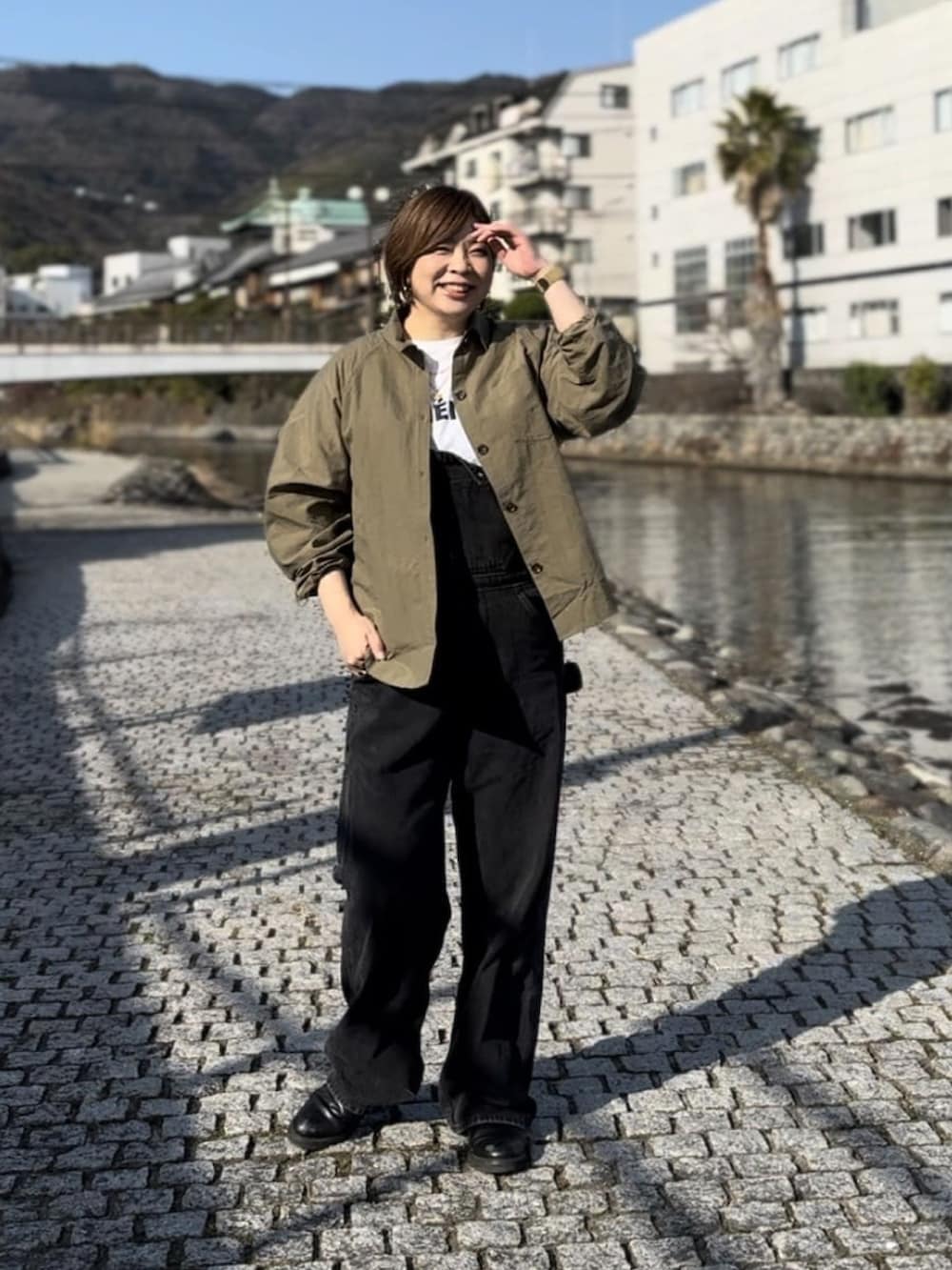 グリーン系のシャツ/ブラウス、ブラック系のサロペット/オーバーオール、ホワイト系のTシャツ/カットソーを着用したレディースの冬コーディネートの2枚目の写真