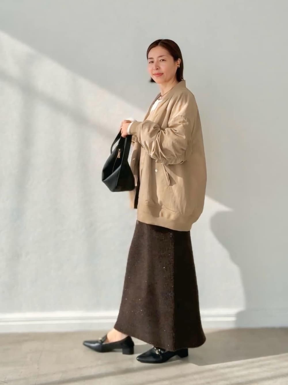 ブラウン系のスカート、ベージュ系のブルゾン、ホワイト系のTシャツ/カットソーを着用したレディースの秋コーディネートの3枚目の写真