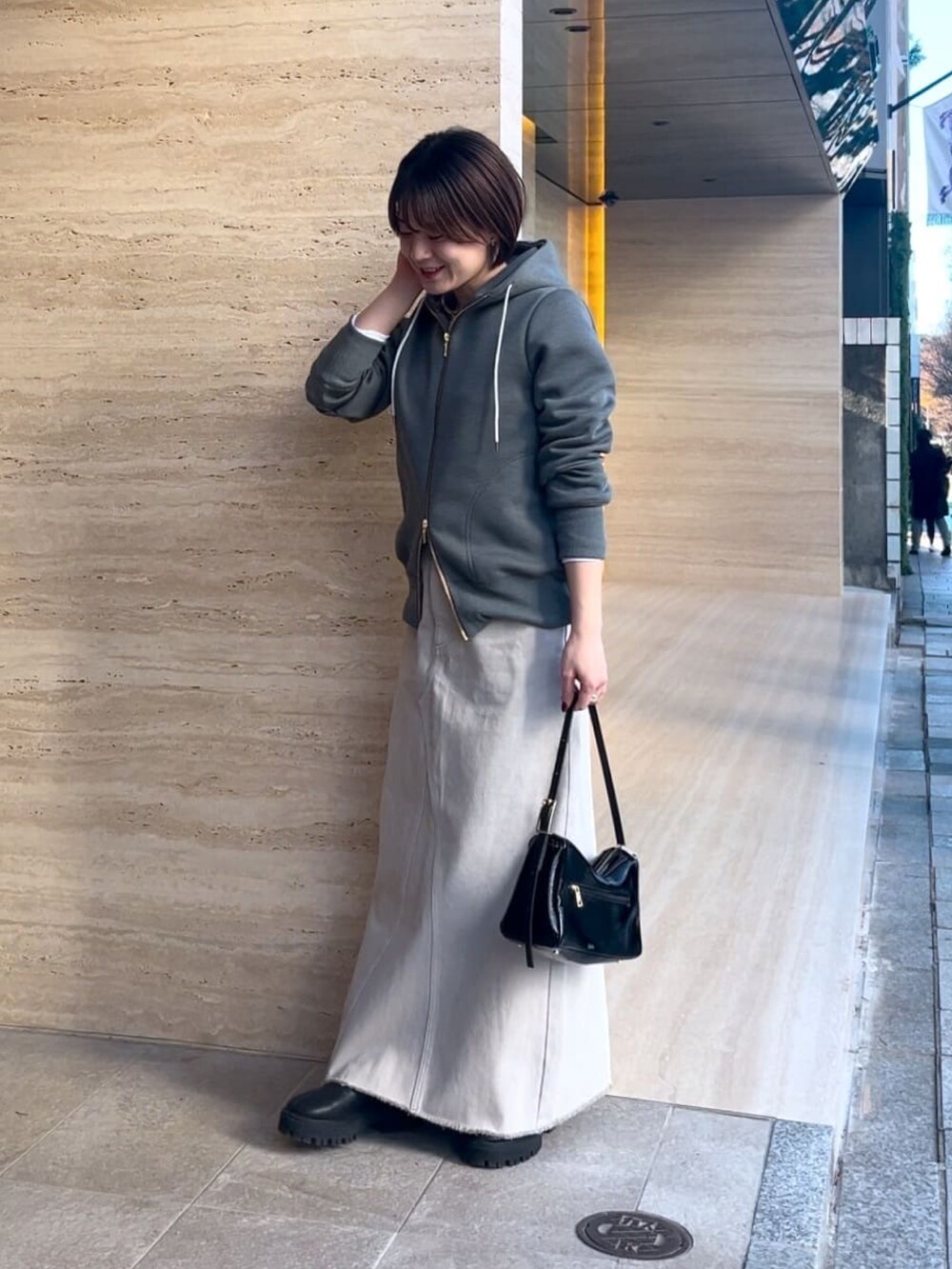 グレー系のパーカー、グレー系のデニムスカート、ブラック系のショルダーバッグを着用したレディースの冬コーディネートの2枚目の写真