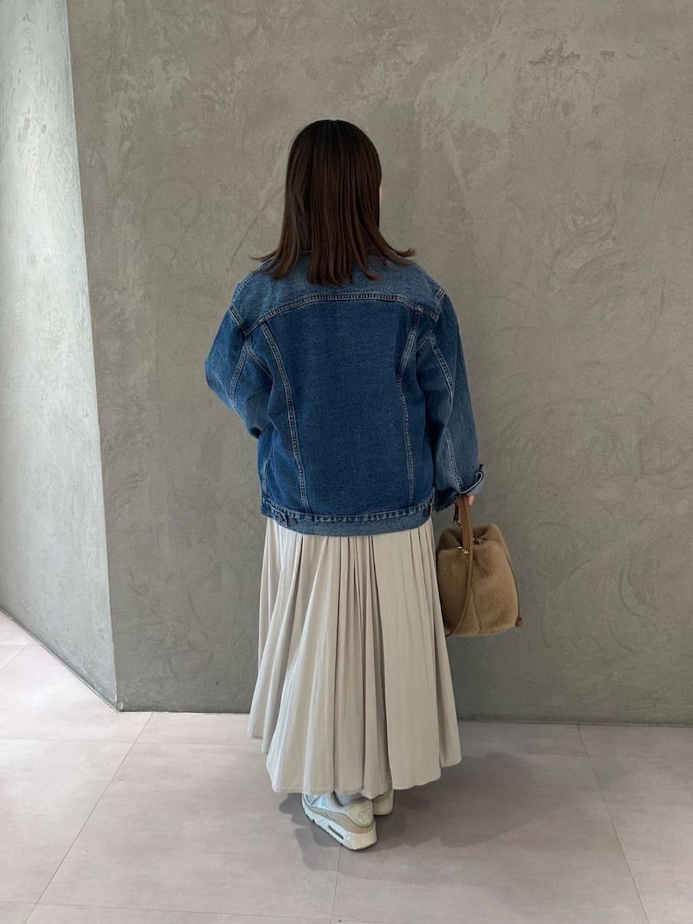 ベージュ系のスカート、ブルー系のデニムジャケット、ベージュ系のハンドバッグを着用したレディースの冬コーディネートの3枚目の写真