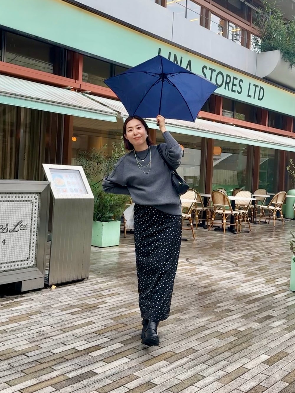 グレー系のニット/セーター、ブラック系のスカート、ブラック系のブーツを着用したレディースの秋コーディネートの2枚目の写真